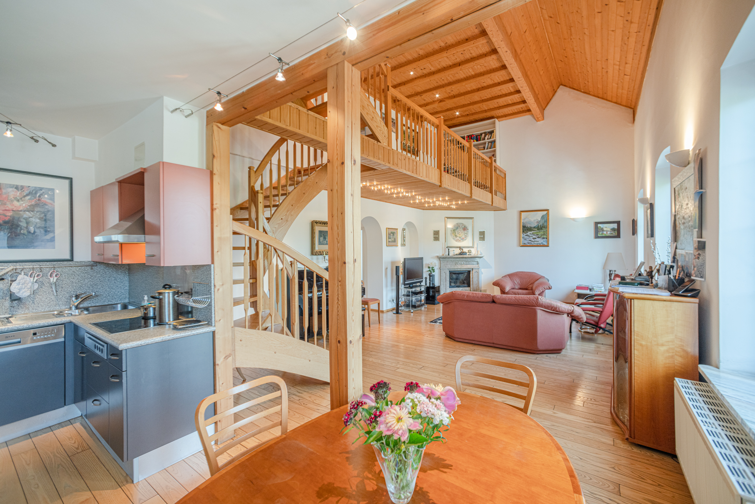 Helles Wohnzimmer mit offener Küche, Holztreppe, Galerie und Ledersofa.