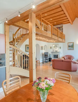 Helles Wohnzimmer mit offener Küche, Holztreppe, Galerie und Ledersofa.