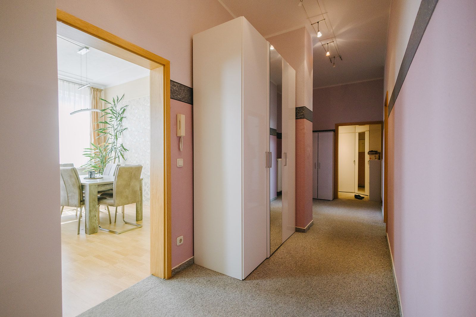 Flur mit Teppichboden, weißen Schränken und Blick in ein Esszimmer mit Tisch und Stühlen.