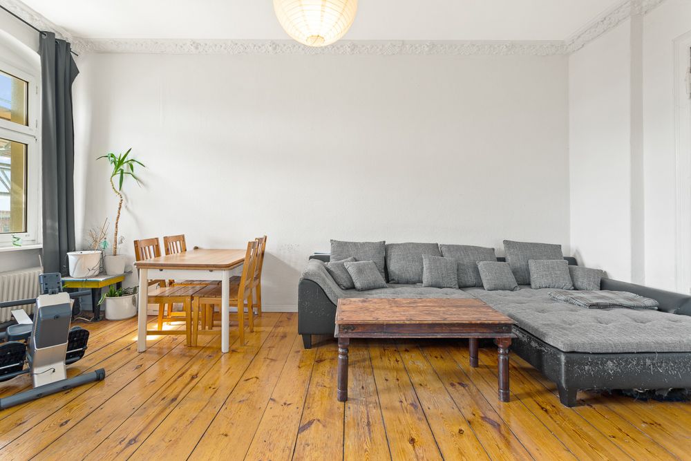 Wohnzimmer mit grauem Sofa, Holztisch, Esstisch mit Stühlen und Pflanzen auf Holzboden.