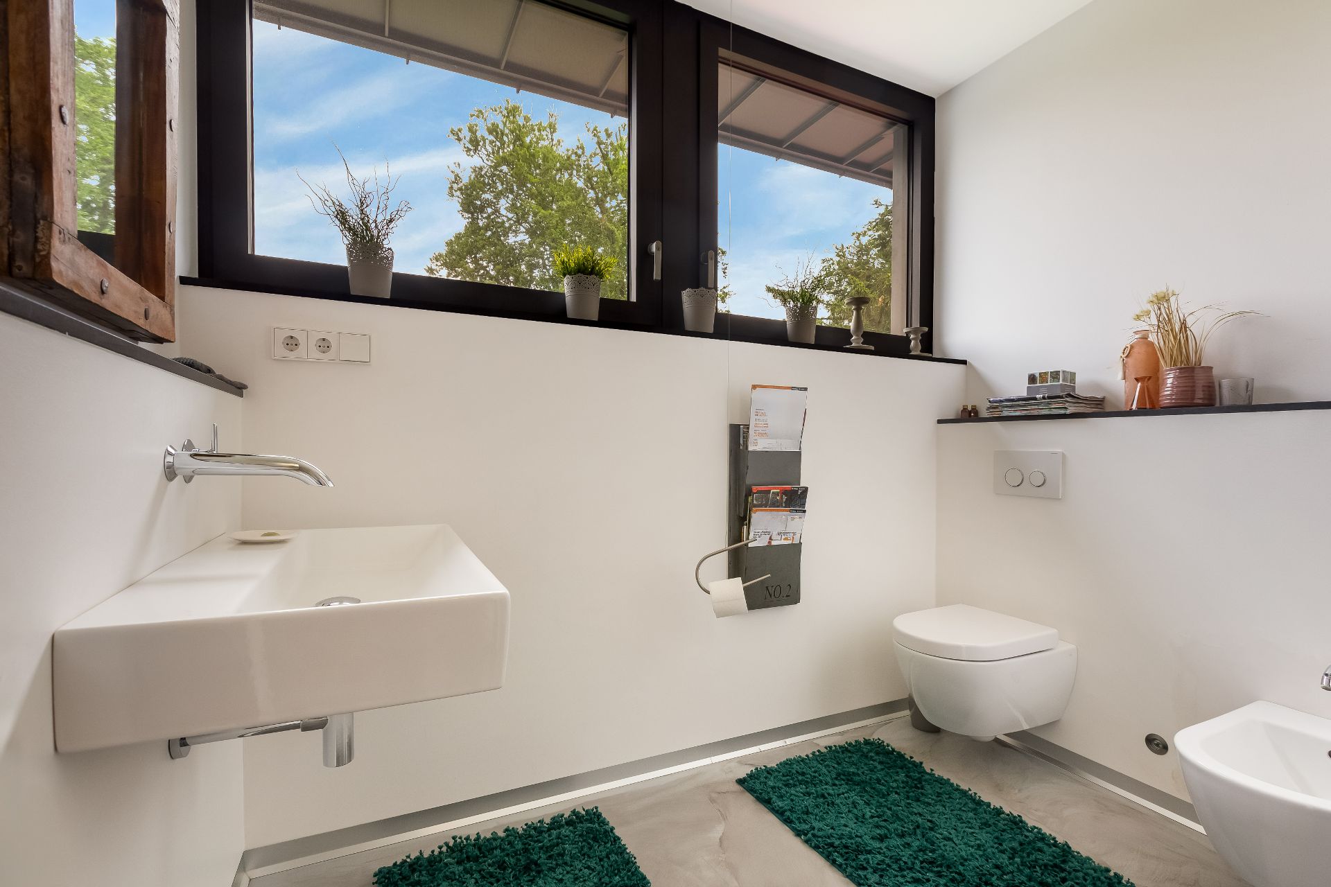 Modernes Badezimmer mit Wandwaschbecken, WC, Zeitschriftenhalter und grünen Teppichen.