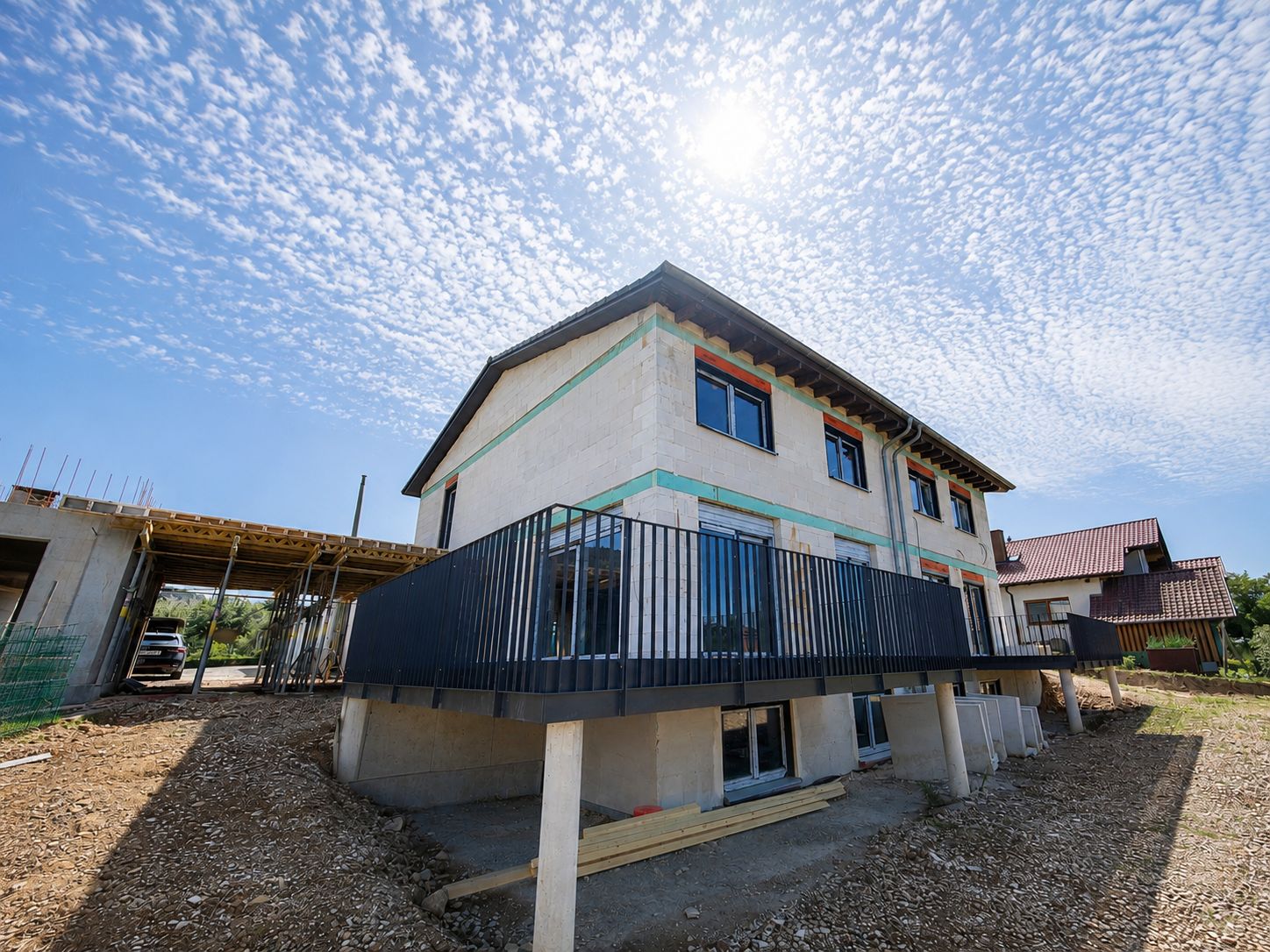 Zweistöckiges Wohnhaus im Bau mit Balkon und großen Fenstern unter blauem Himmel.