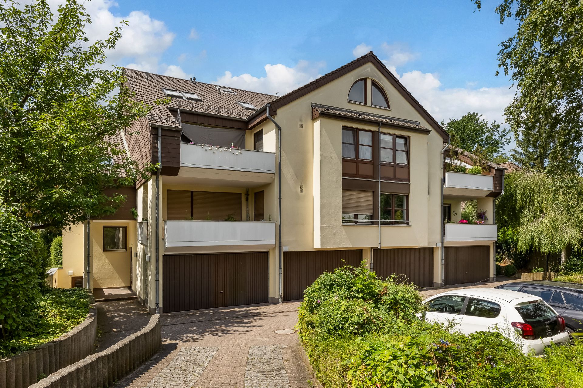 Mehrfamilienhaus mit Balkonen, Garagen und geparkten Autos vor dem Gebäude.