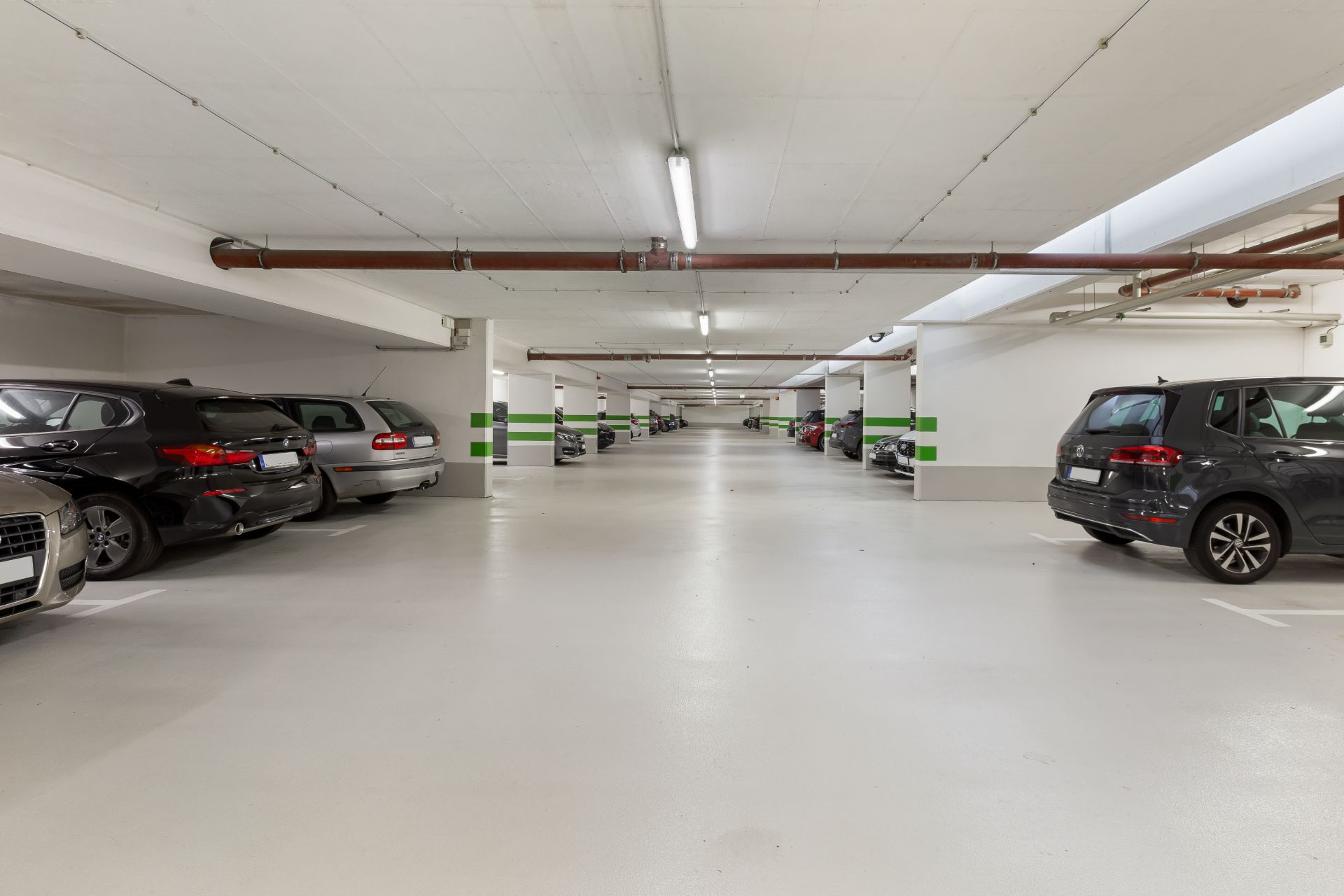 Helle Tiefgarage mit mehreren geparkten Autos und weißen Wänden.