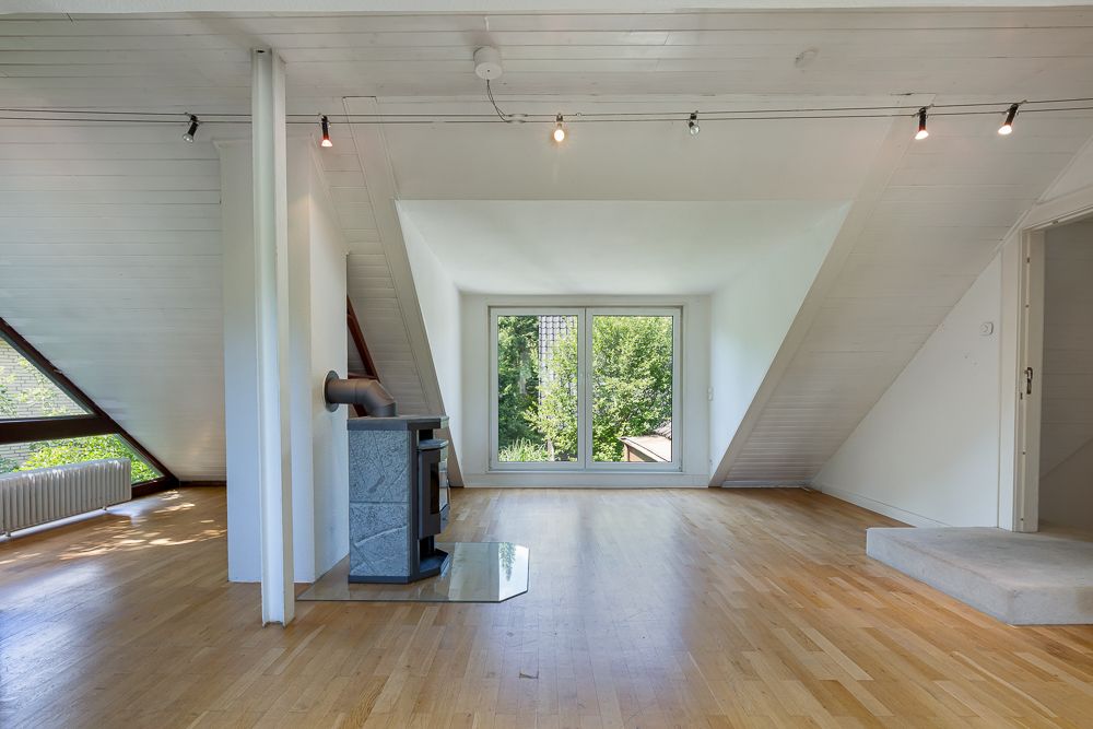Helles Dachzimmer mit großem Fenster, Holzfußboden und Kaminofen.