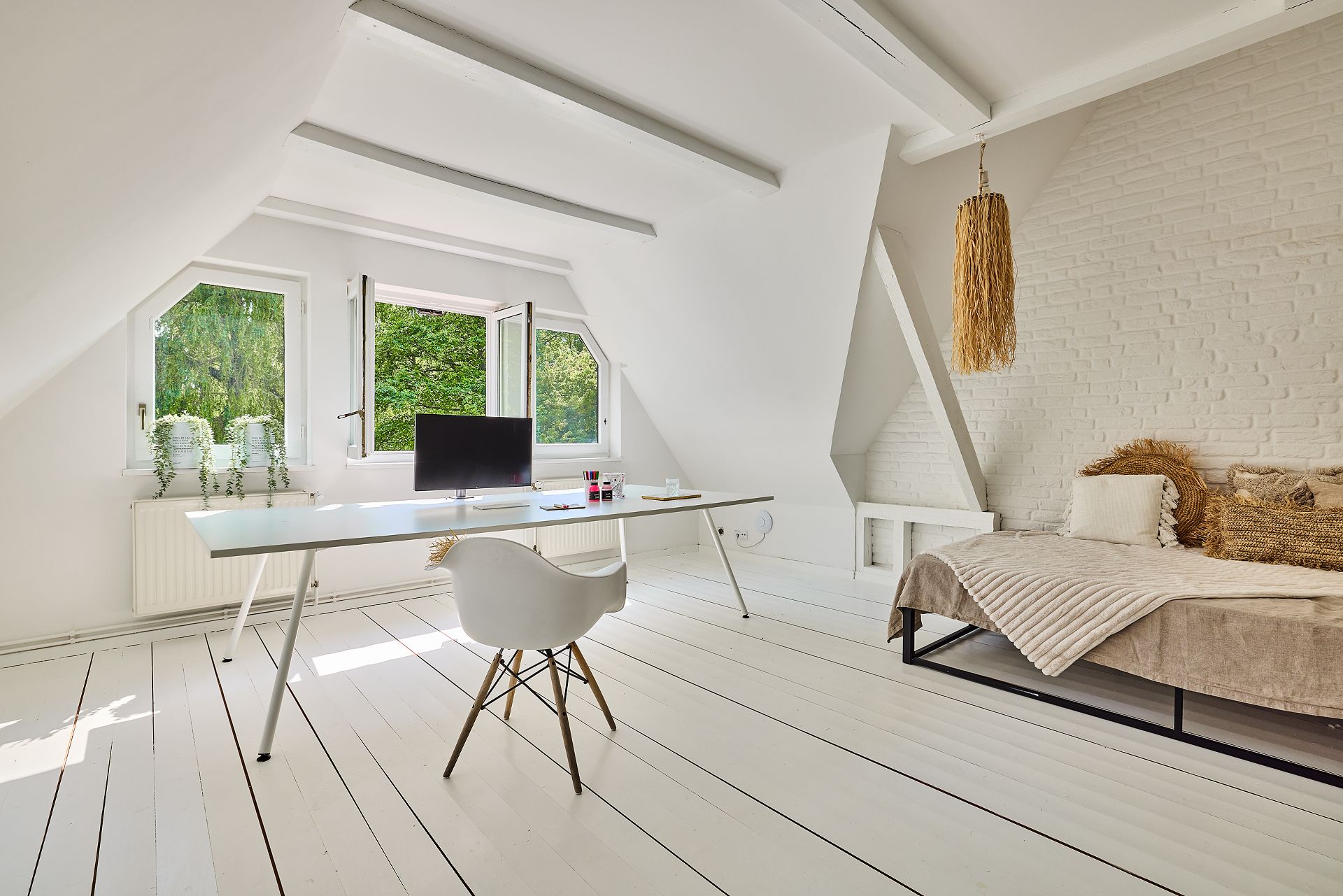 Helles Zimmer mit Schreibtisch, Computer, Stuhl, Bett und weißen Holzböden.