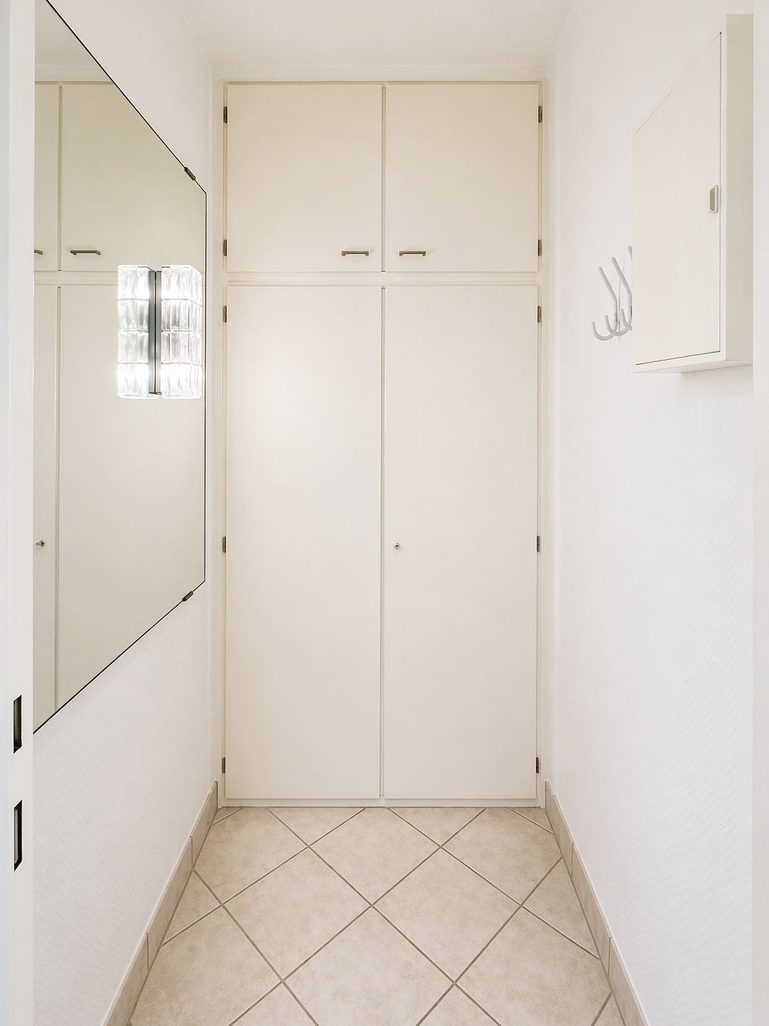 Heller Flur mit großem Spiegel, weiße Einbauschränke und Haken an der Wand.