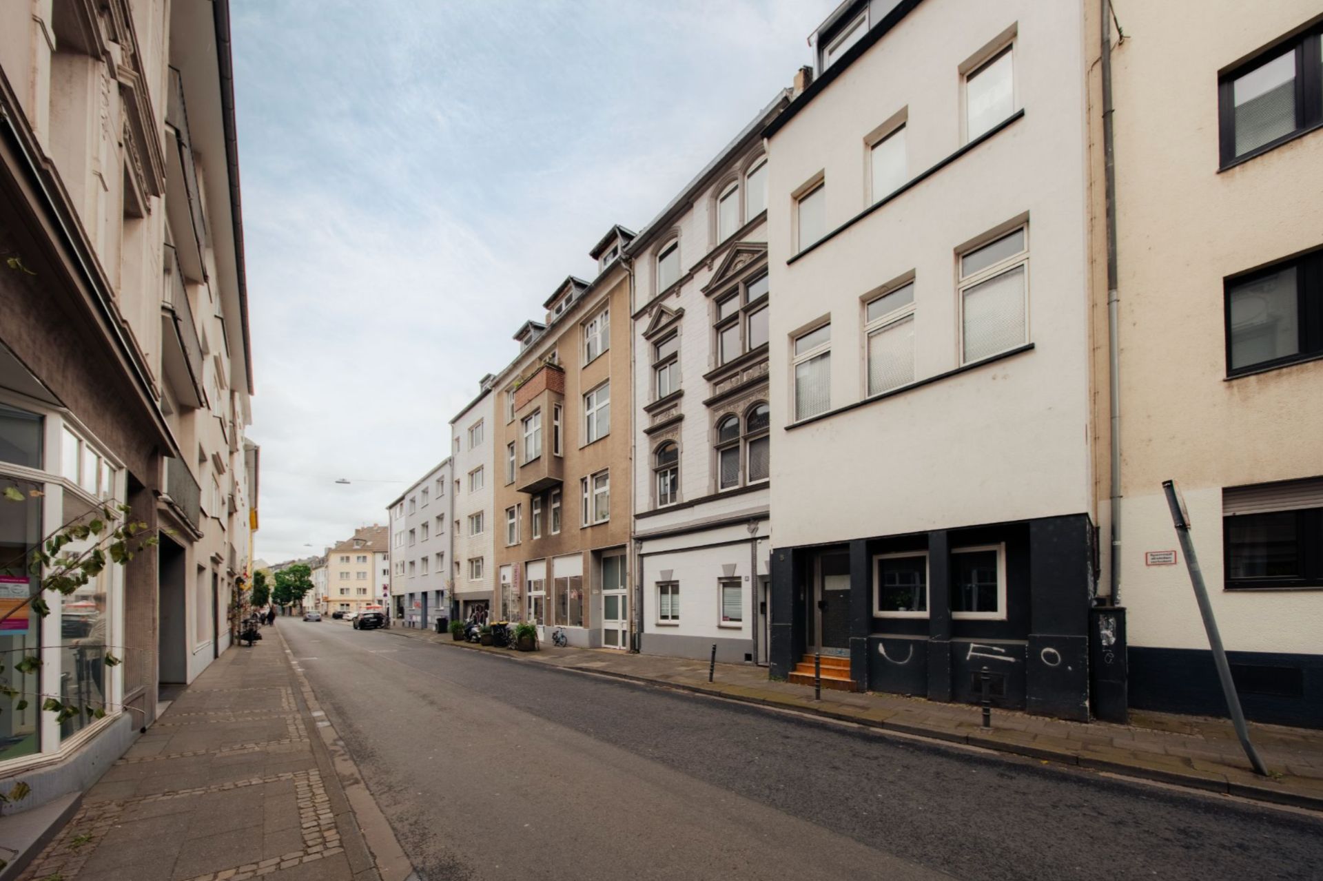 Wohnstraße mit mehrstöckigen Wohnhäusern und Gehweg bei Tageslicht.