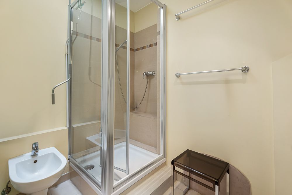 Modernes Bad mit Glasdusche, Bidet, Handtuchhalter und kleinem Regal auf beigem Boden.