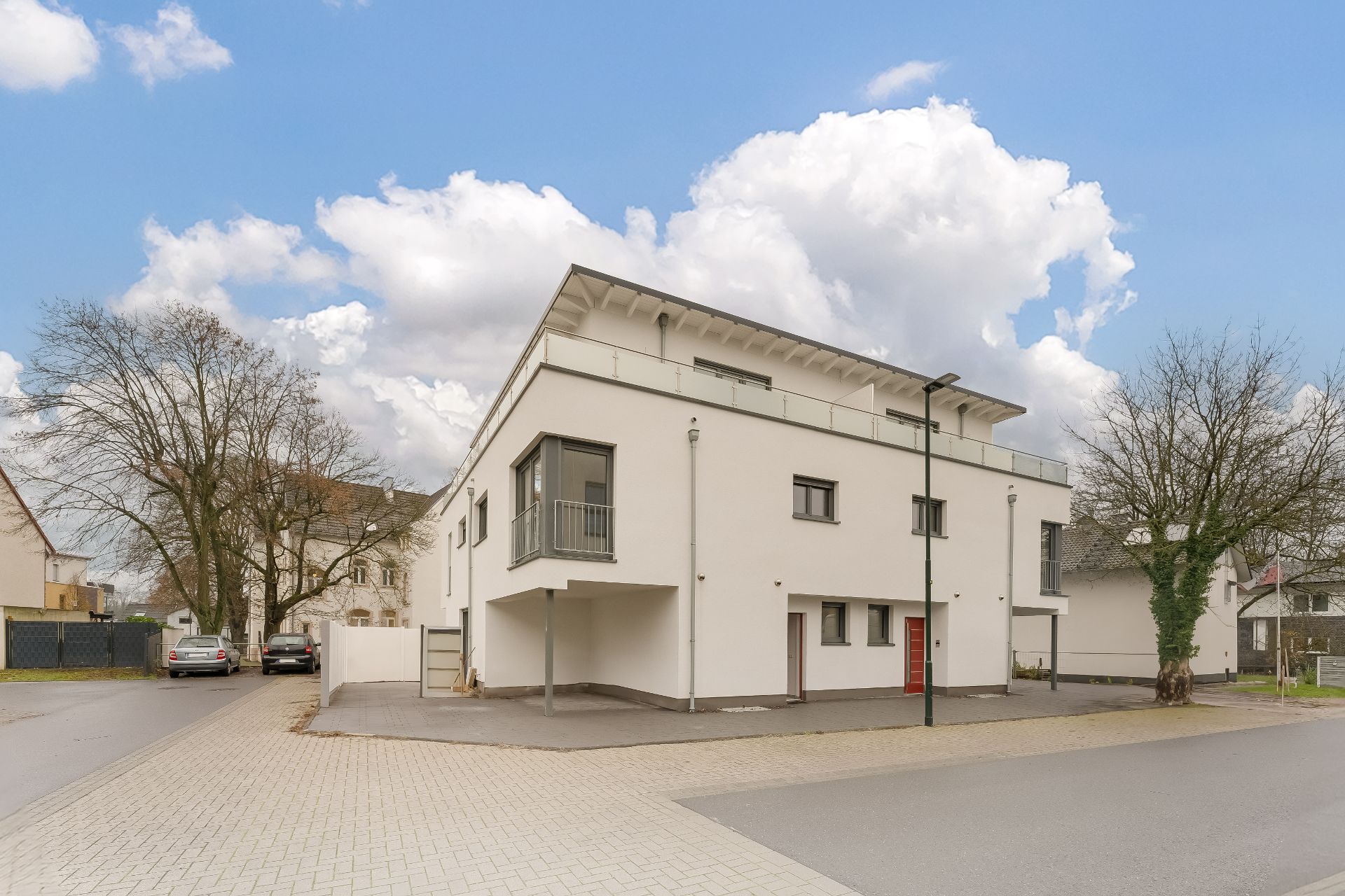 Modernes, weißes Wohnhaus mit Flachdach und großen Fenstern an einer Straßenecke.