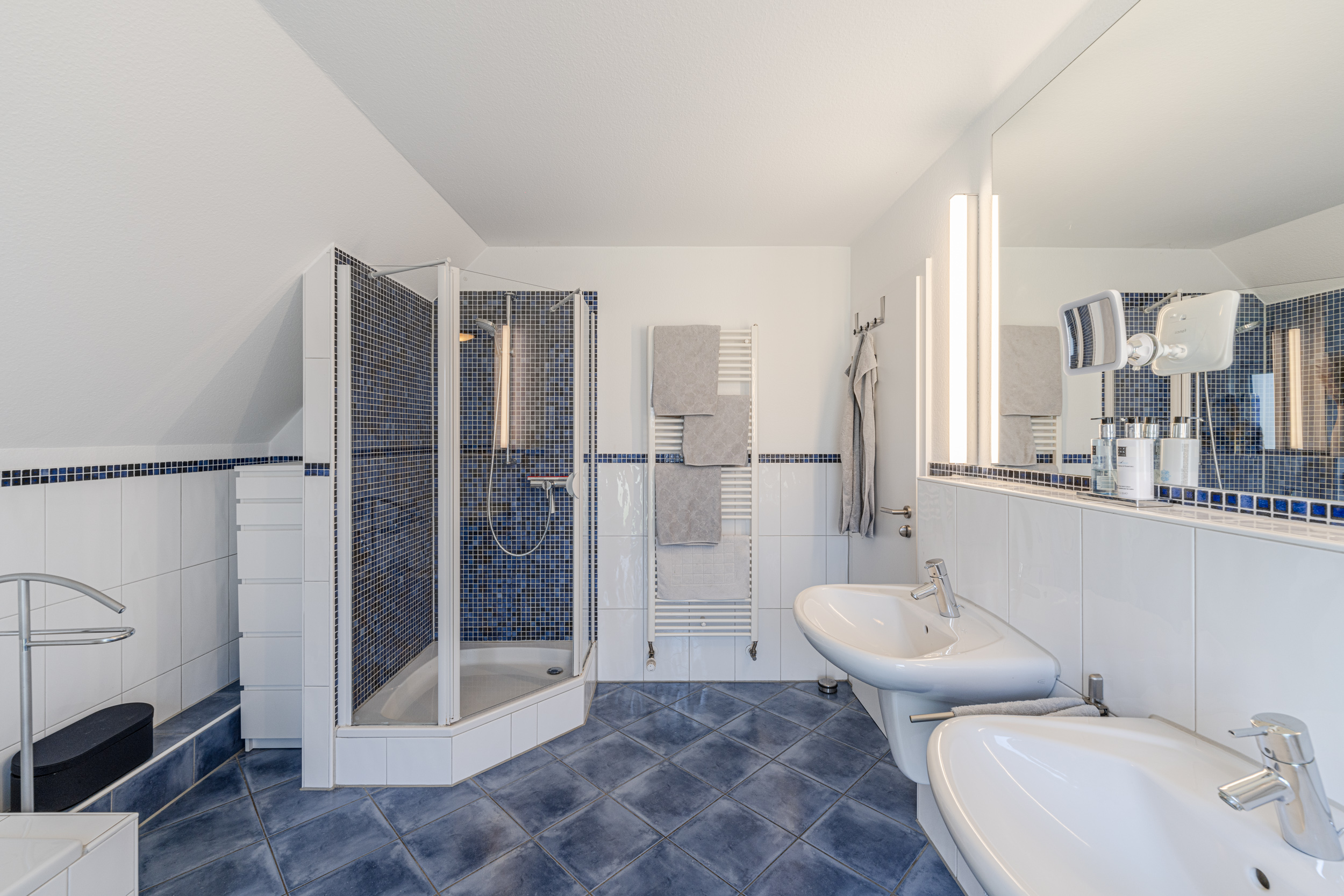 Modernes Badezimmer mit Dusche, zwei Waschbecken, Spiegel und blauen Fliesen.