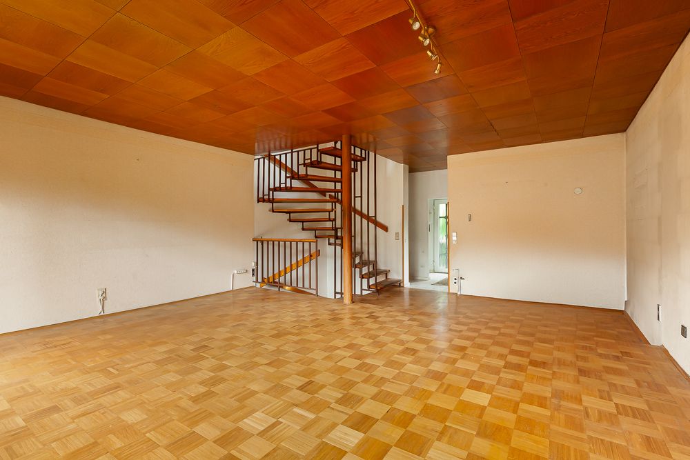 Leeres Wohnzimmer mit Holzdecke, Parkettboden und offener Holztreppe.