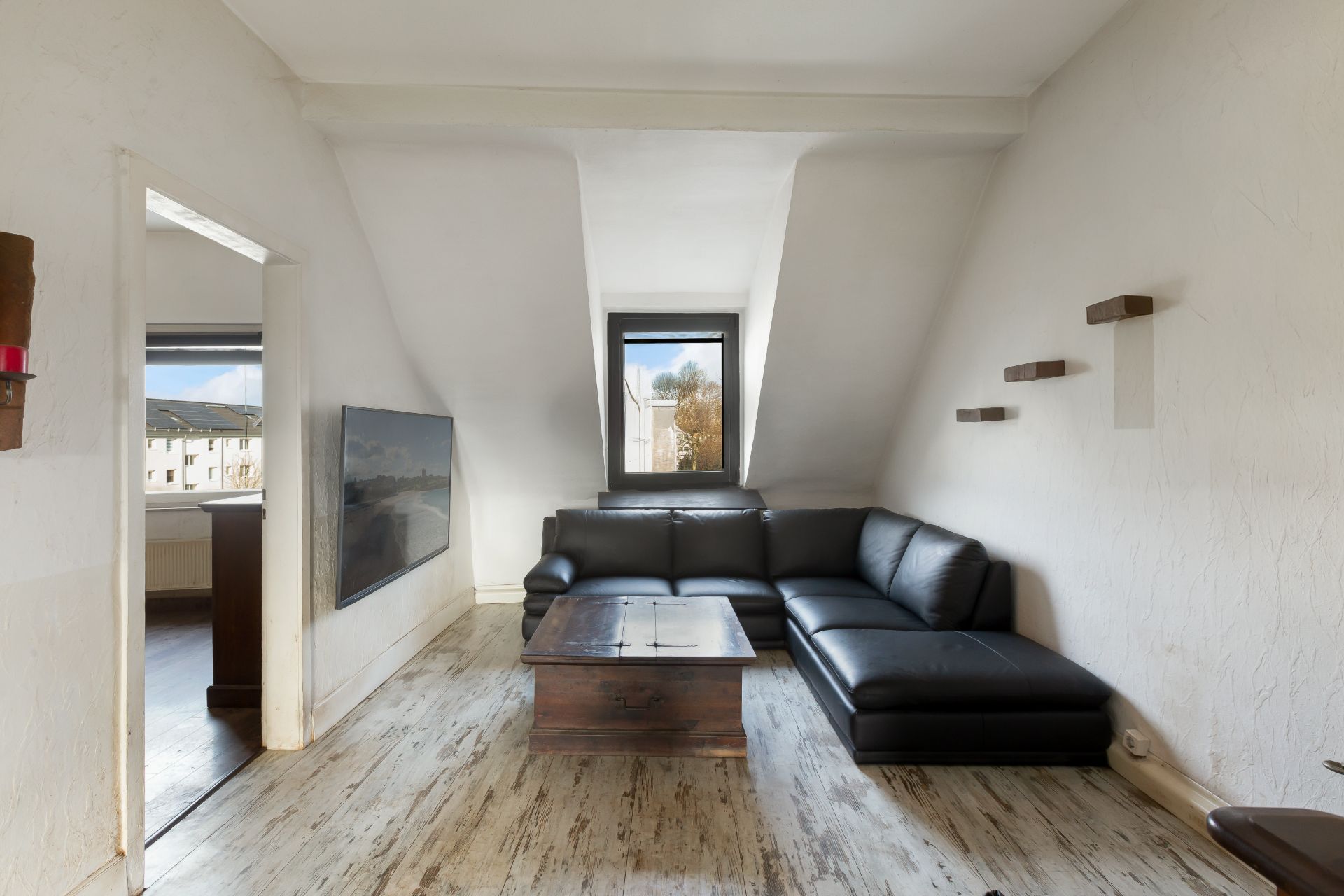 Helles Wohnzimmer mit schwarzem Ecksofa, Holztisch, Wandregalen und Fenster.