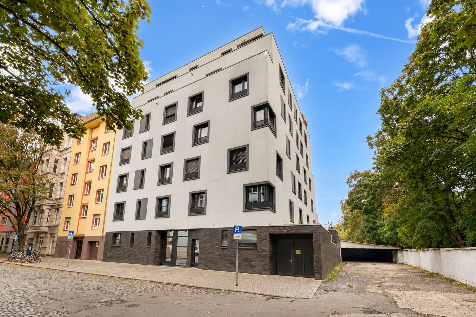 Sechsstöckiges Wohnhaus mit weißen und dunklen Fassadenelementen, umgeben von Bäumen.