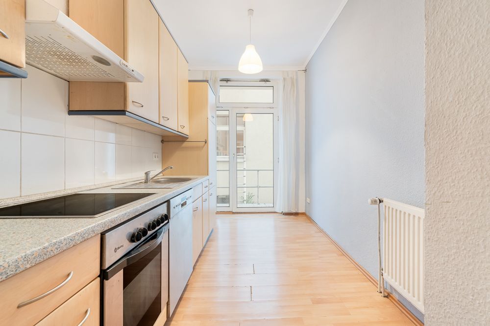 Helle Einbauküche mit Herd, Spüle und Zugang zu einem Balkon im Hintergrund.