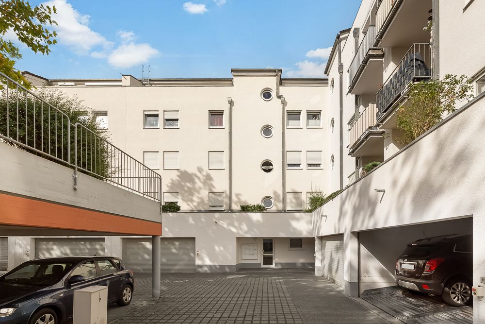 Innenhof eines Wohngebäudes mit Garagen, geparkten Autos und Balkonen, umgeben von weißen Fassaden.