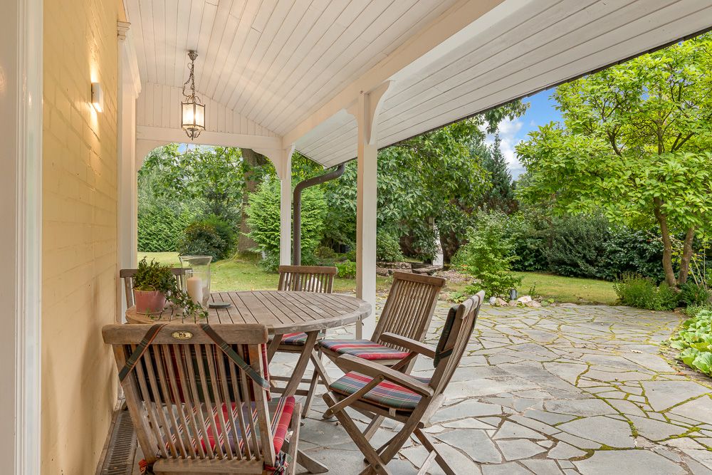 Überdachte Terrasse mit Holztisch und Stühlen, Blick in einen grünen Garten.