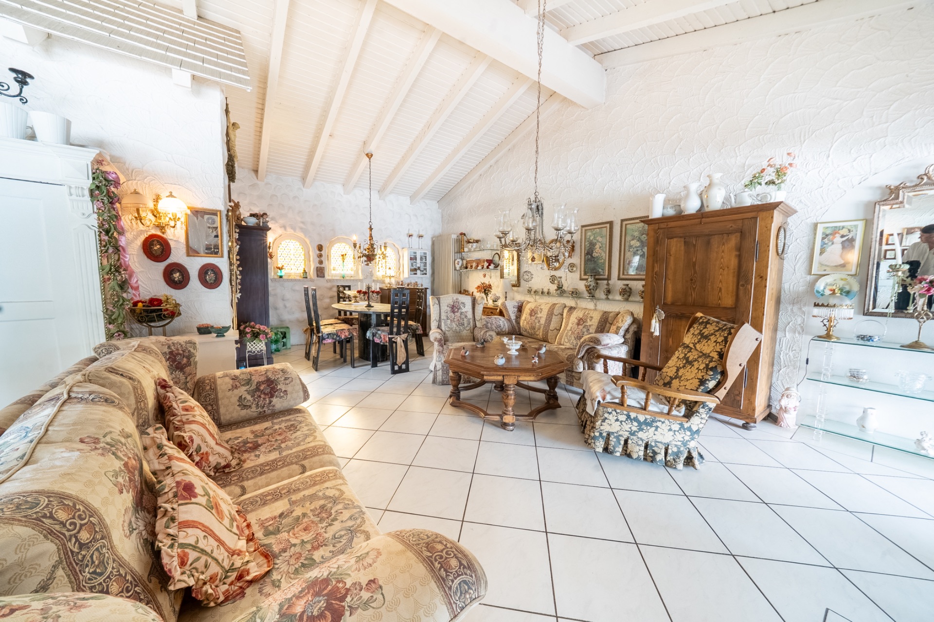 Helles Wohnzimmer mit gemusterten Sofas, Holzmöbeln, Bildern an der Wand und vielen Dekorationen.