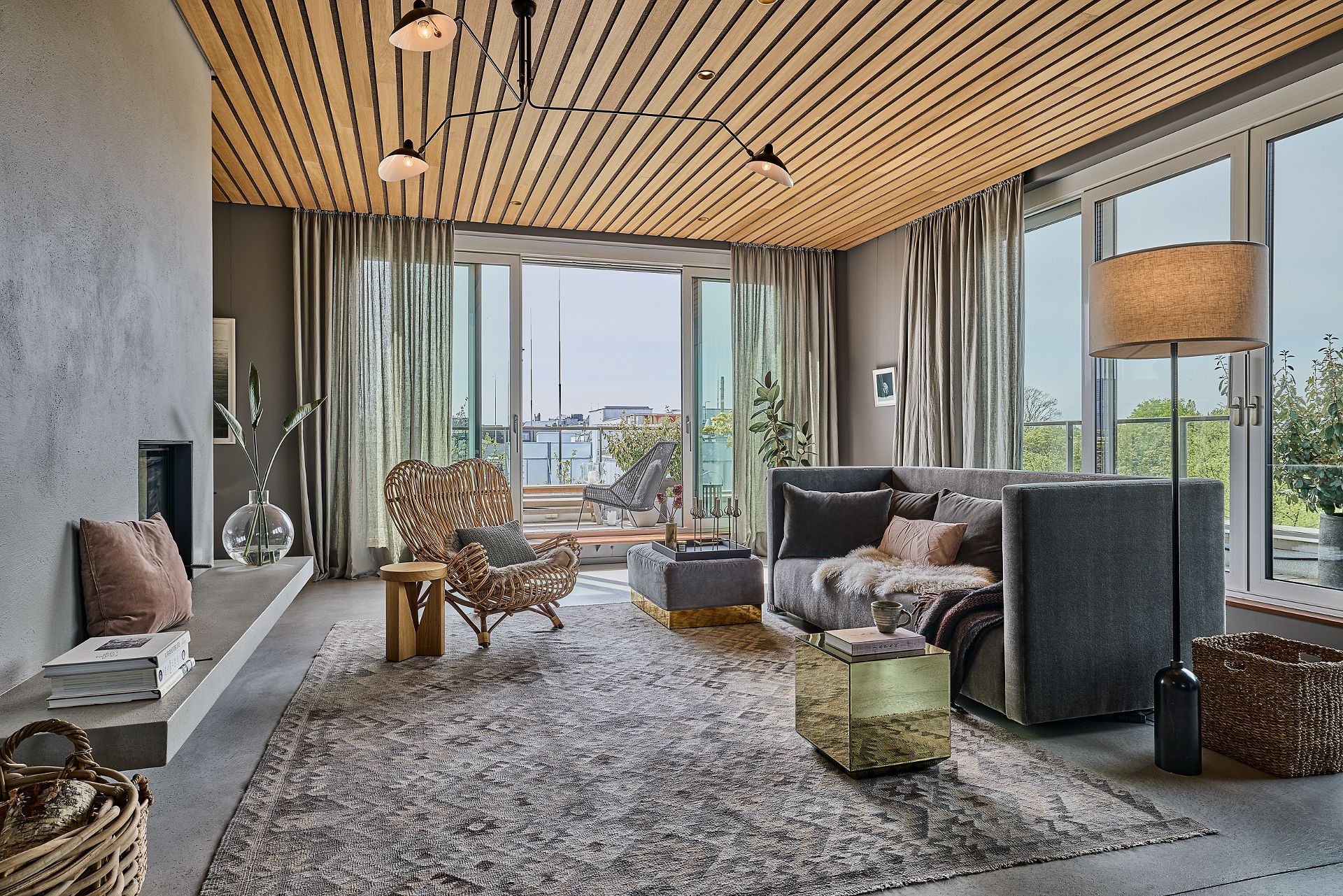 Modernes Wohnzimmer mit grauem Sofa, Kamin, Sessel und großen Fenstern zu einem Balkon.