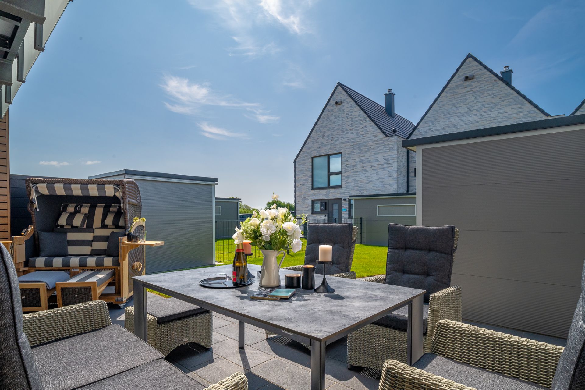 Moderne Terrasse mit Sitzgruppe, Tisch, Blumen, Kerzen und Ausblick auf Wohnhäuser.