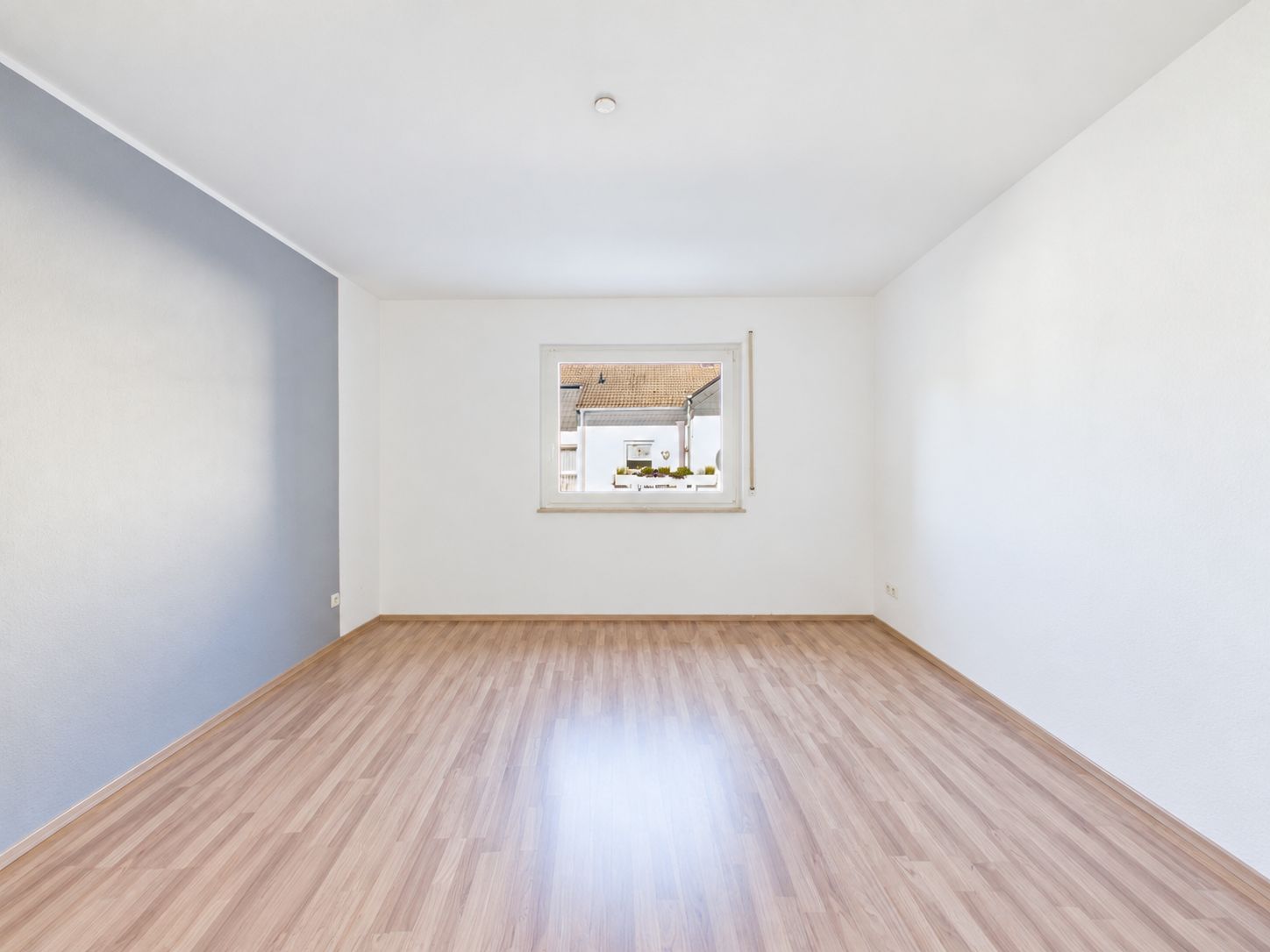 Leerer Raum mit Holzfußboden, weißen Wänden und einem Fenster zur Straße.