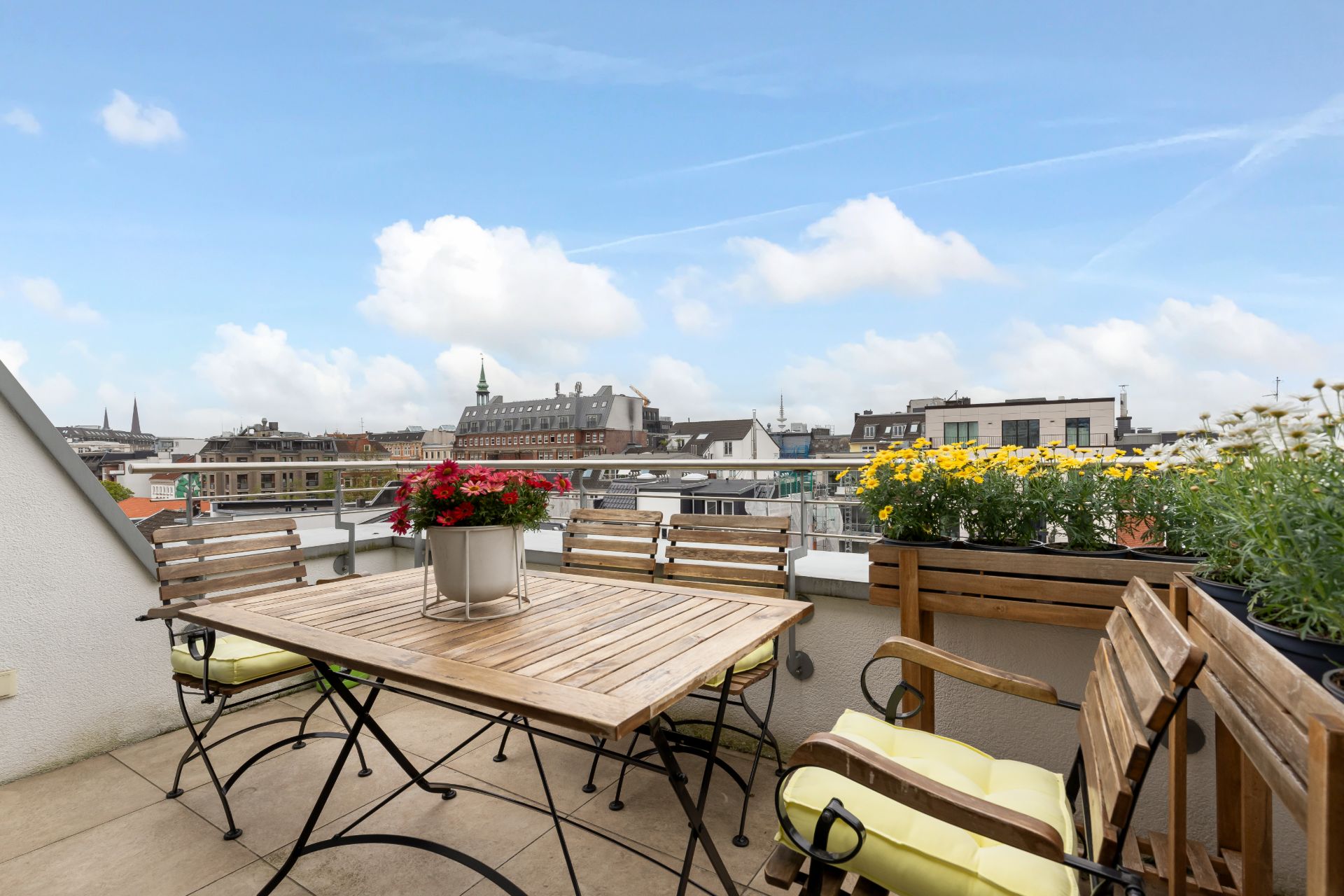 Balkon mit Holztisch, Stühlen und Blumenkästen, Blick auf Stadtgebäude.