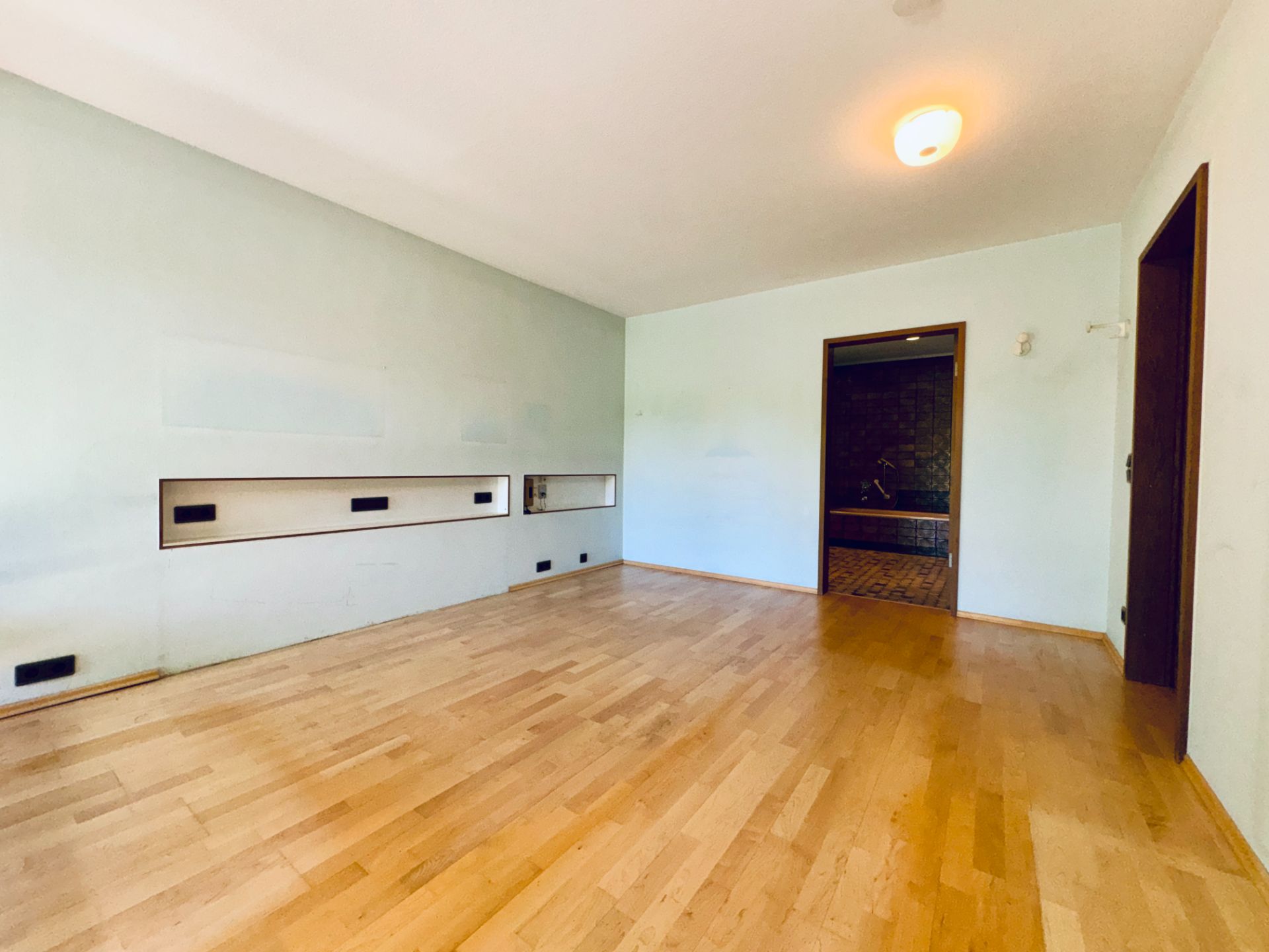 Helles Zimmer mit Holzfußboden, weißer Wand und eingebauten Wandfächern.