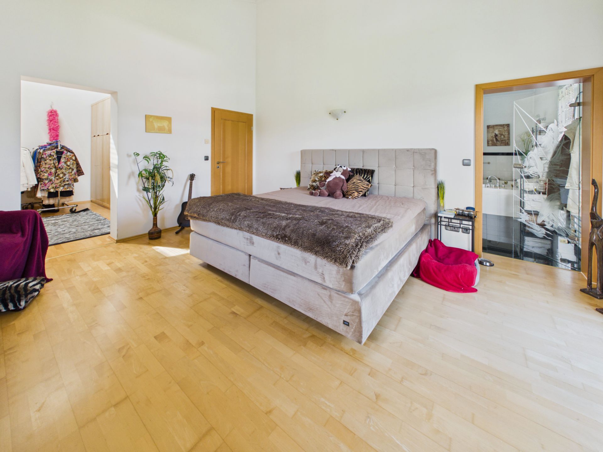Helles Schlafzimmer mit großem Bett, Holzboden und Zugang zu Ankleide- und Nebenraum.