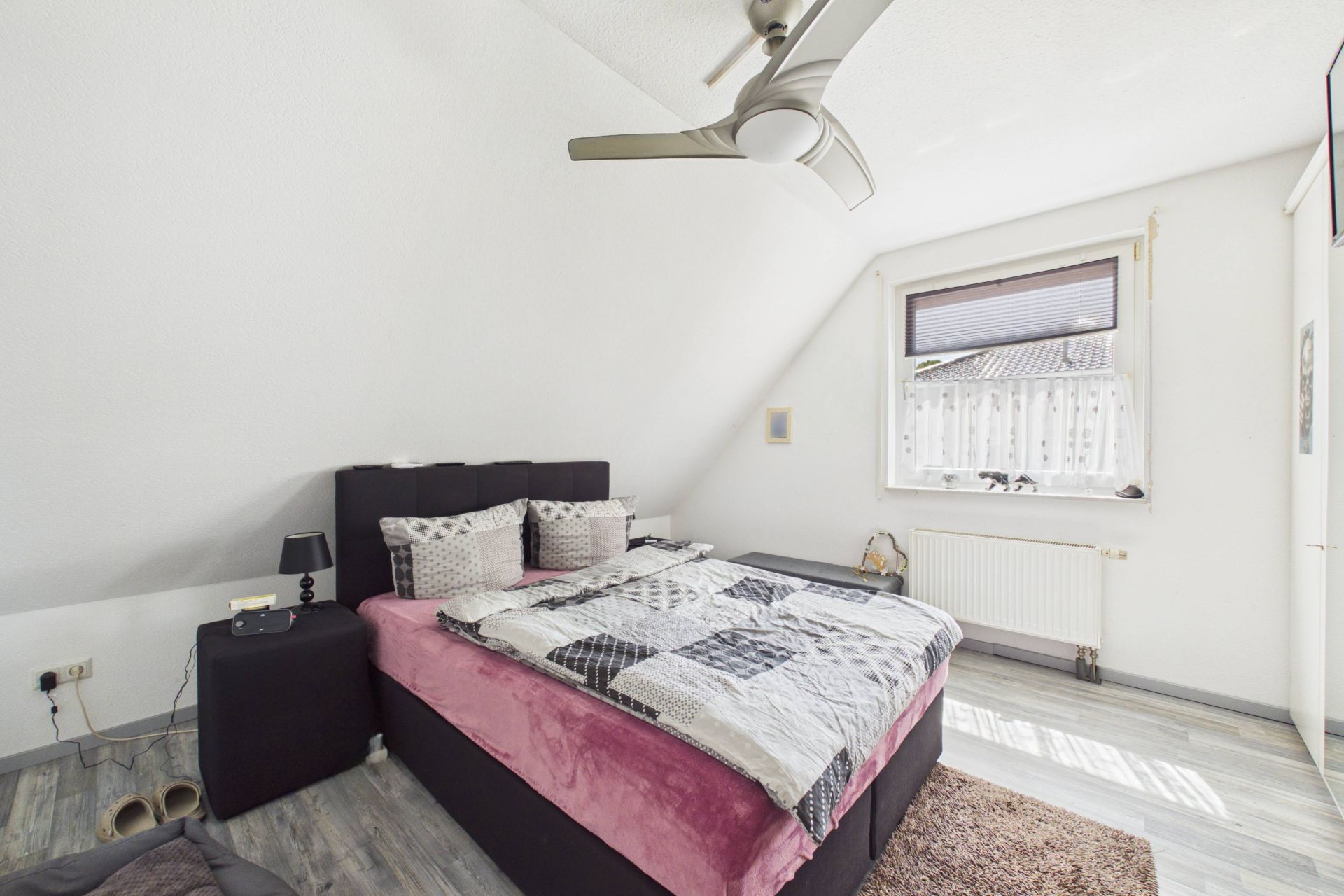 Schlafzimmer mit Doppelbett, Nachttisch, Fenster und Deckenventilator.