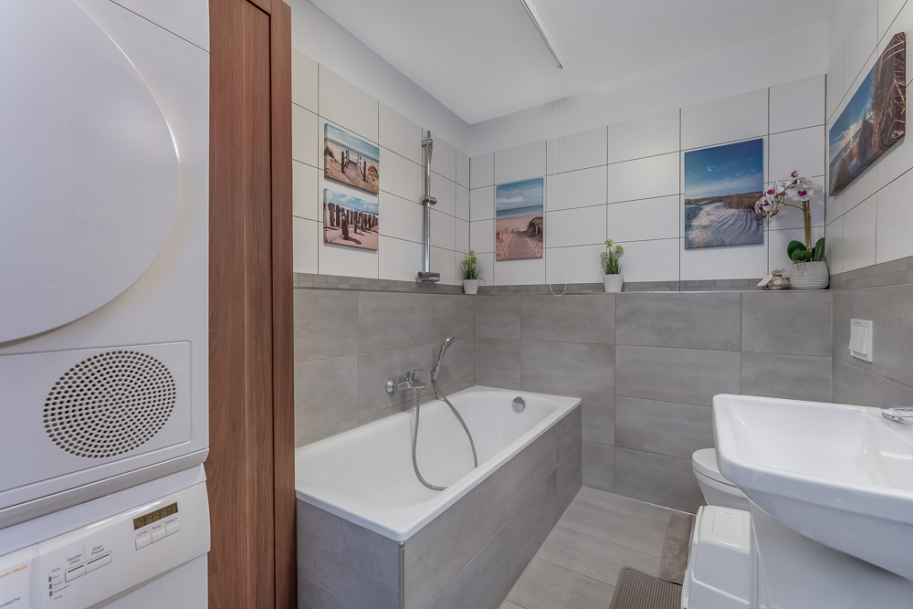 Modernes Badezimmer mit Badewanne, Waschbecken, WC, Waschmaschine und Bildern an den Wänden.