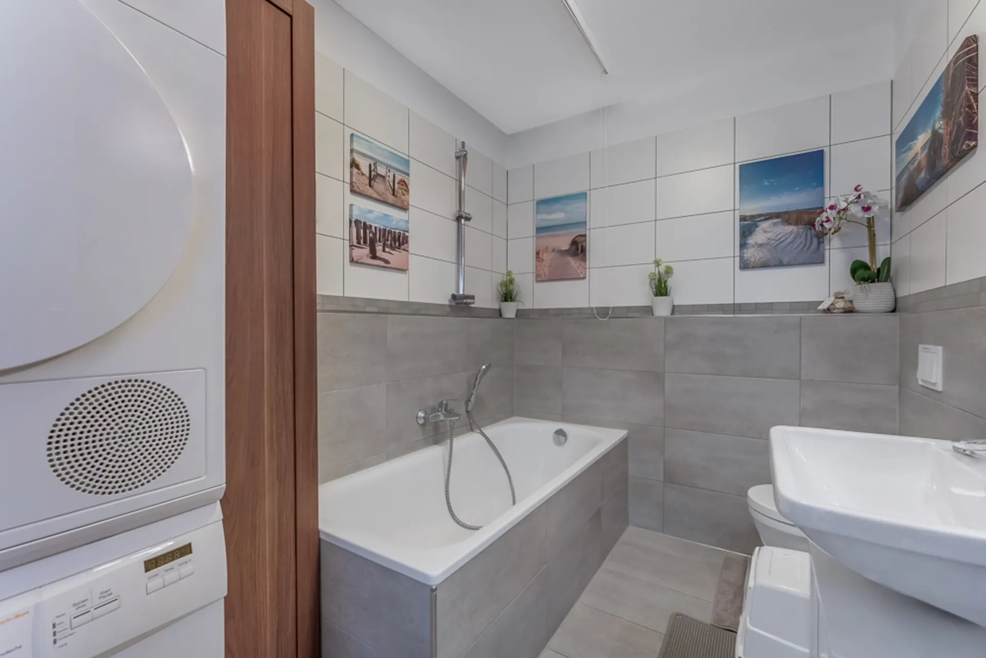 Modernes Badezimmer mit Badewanne, Waschbecken, WC, Waschmaschine und Bildern an den Wänden.
