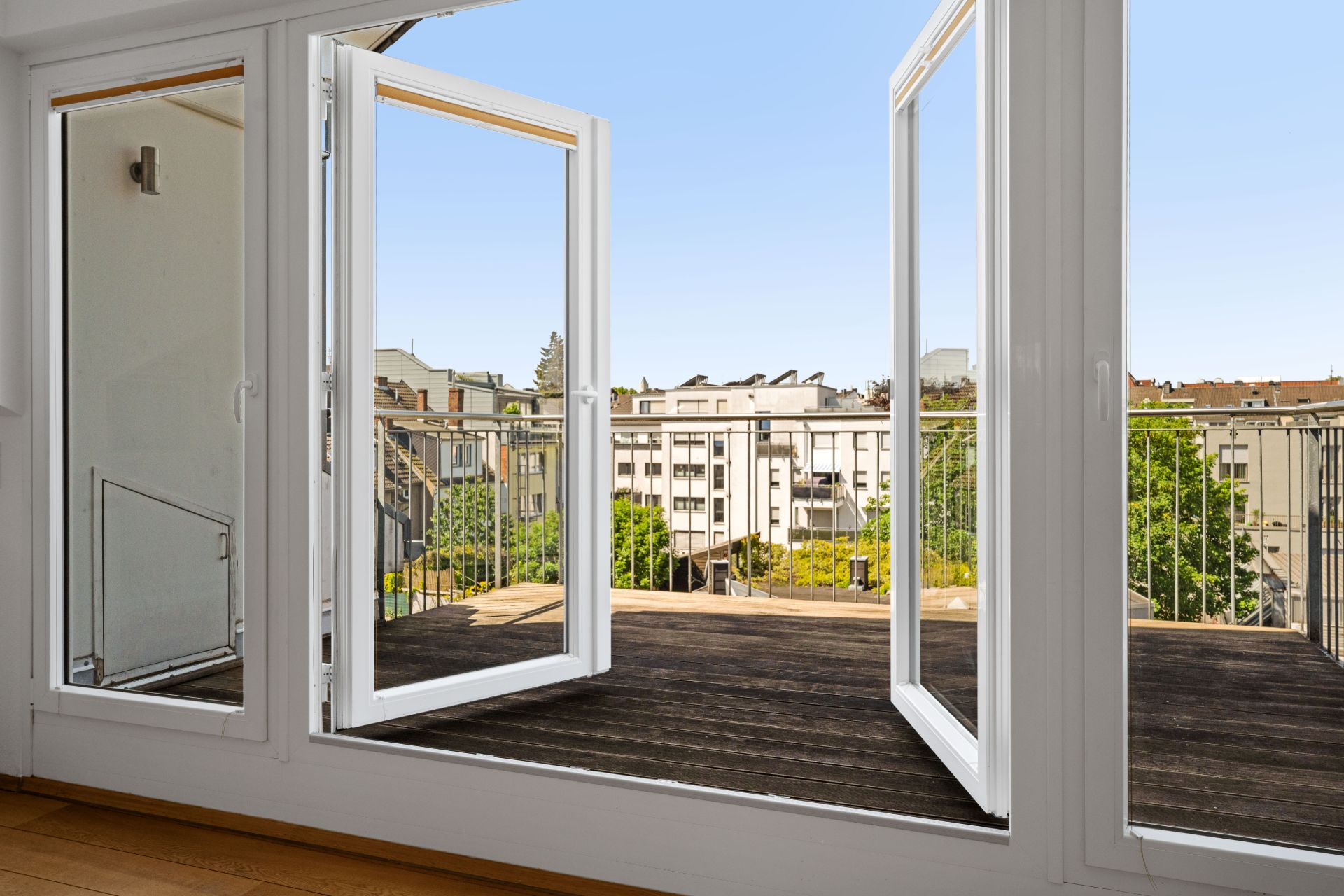 Offene Glastüren führen von einem Zimmer auf einen großen Balkon mit Blick auf andere Wohnhäuser.