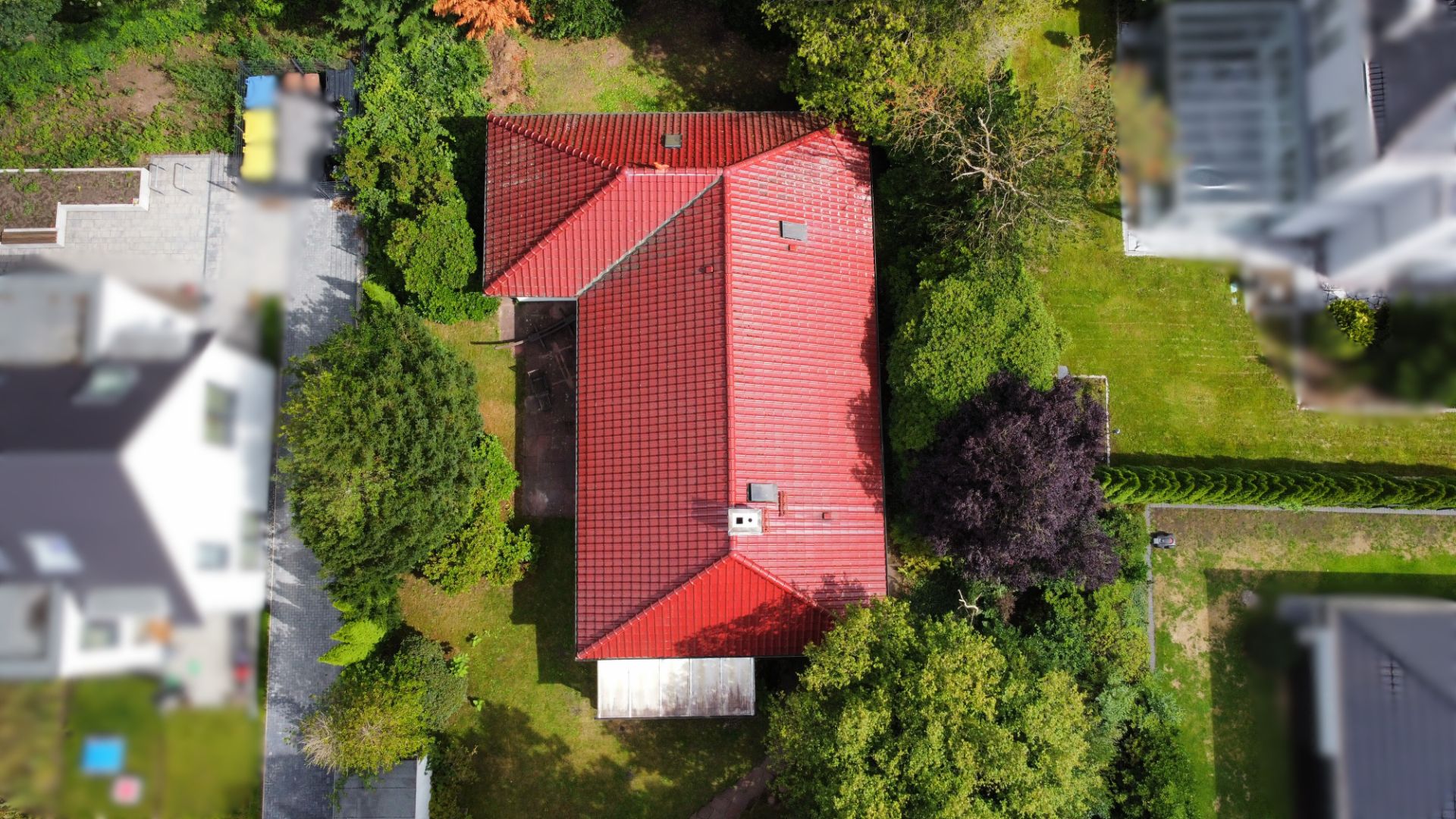 Luftaufnahme eines Hauses mit rotem Dach, umgeben von Garten und Bäumen.