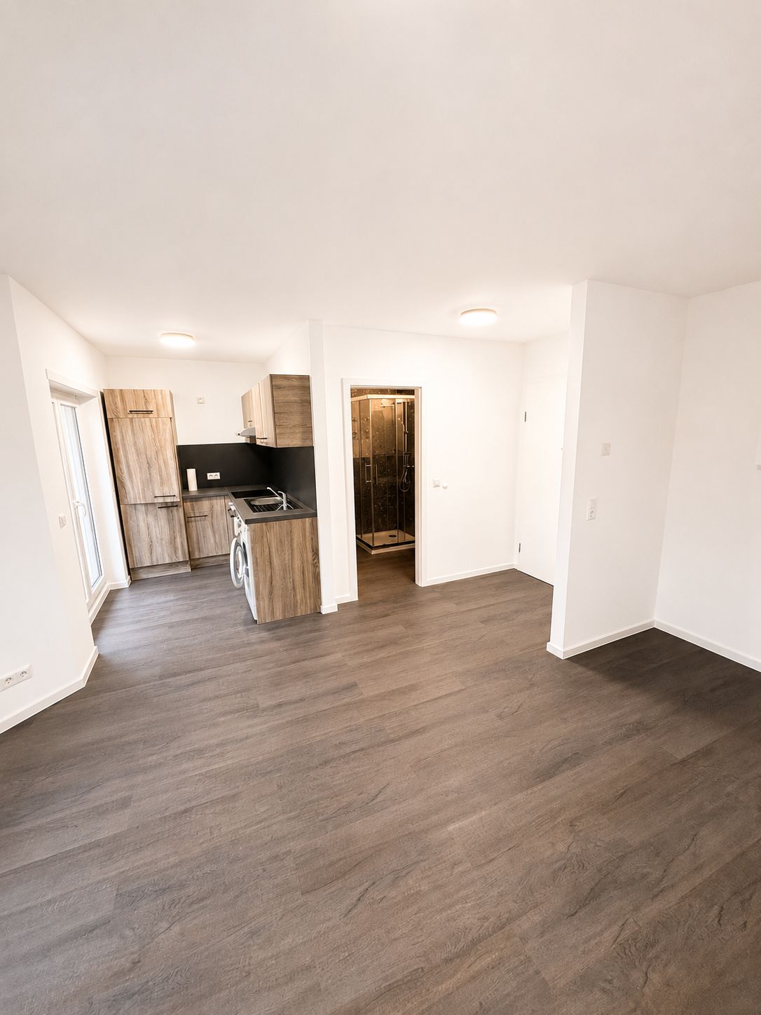 Heller Raum mit Holzfußboden, offener Küche und Zugang zum Badezimmer.