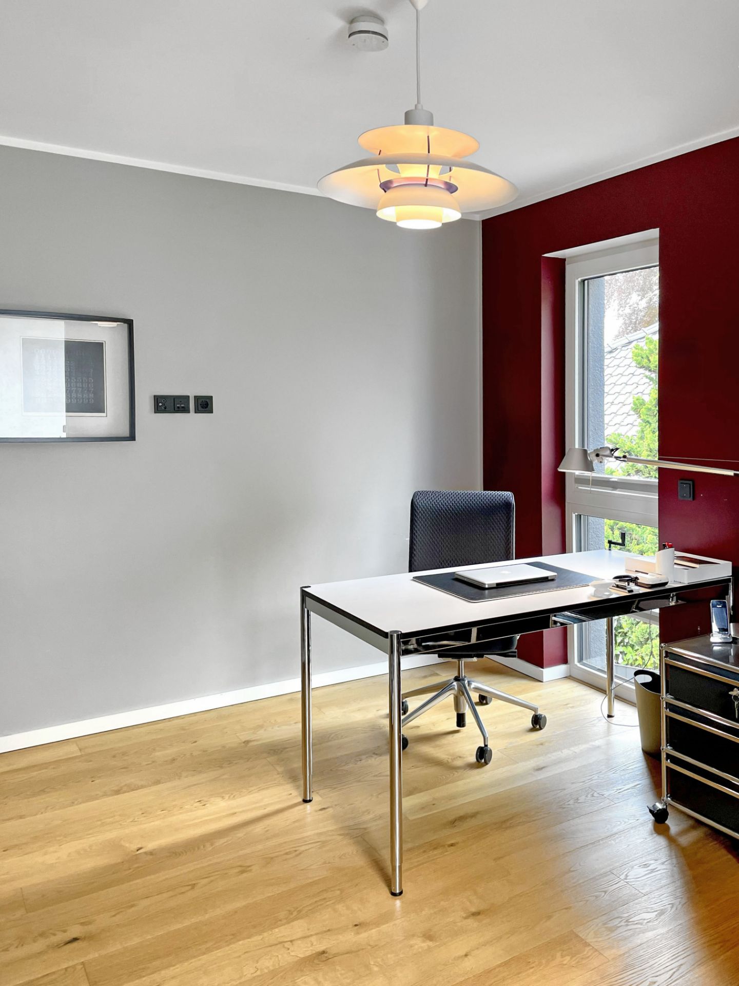 Modernes Arbeitszimmer mit Schreibtisch, Stuhl, Hängelampe und großem Fenster auf Holzfußboden.