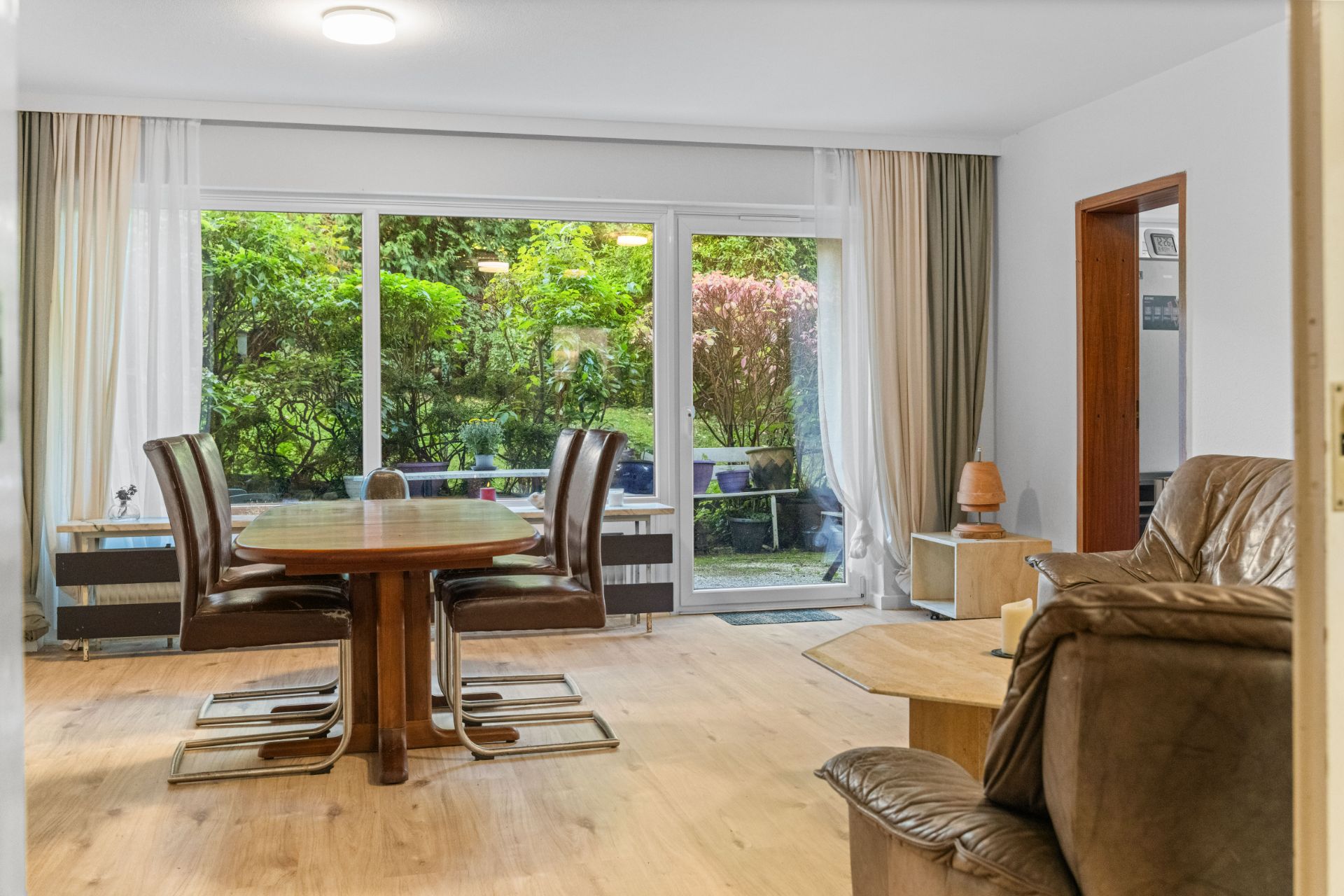 Helles Wohnzimmer mit Esstisch, Stühlen und Ledersofa, großer Fensterfront zum Garten.