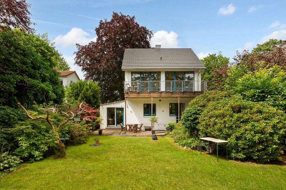 Zweistöckiges Wohnhaus mit Balkon und großem Garten, umgeben von Bäumen und Sträuchern.