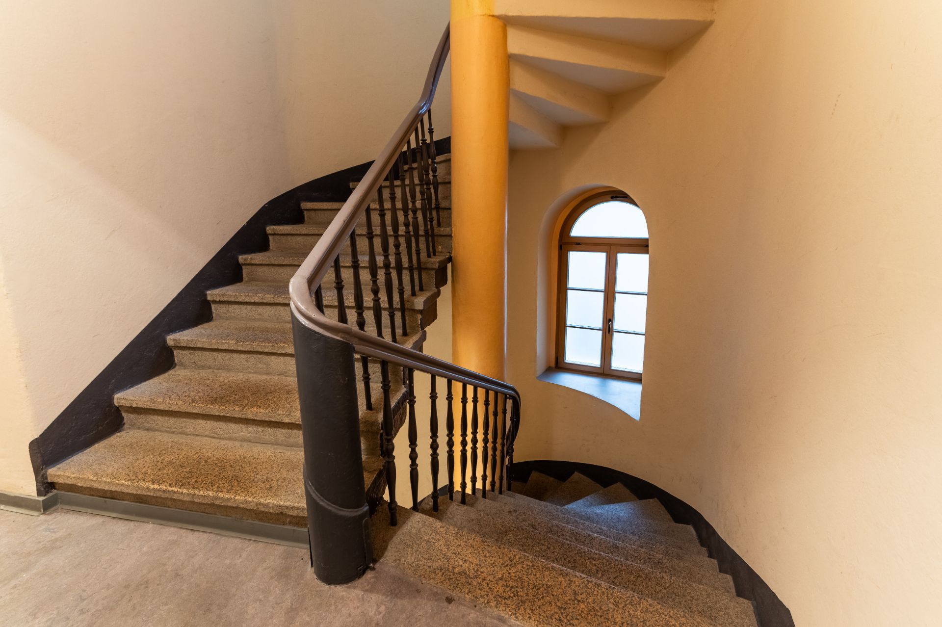 Steintreppe mit Geländer und Fenster mit Holzrahmen an der Wand.