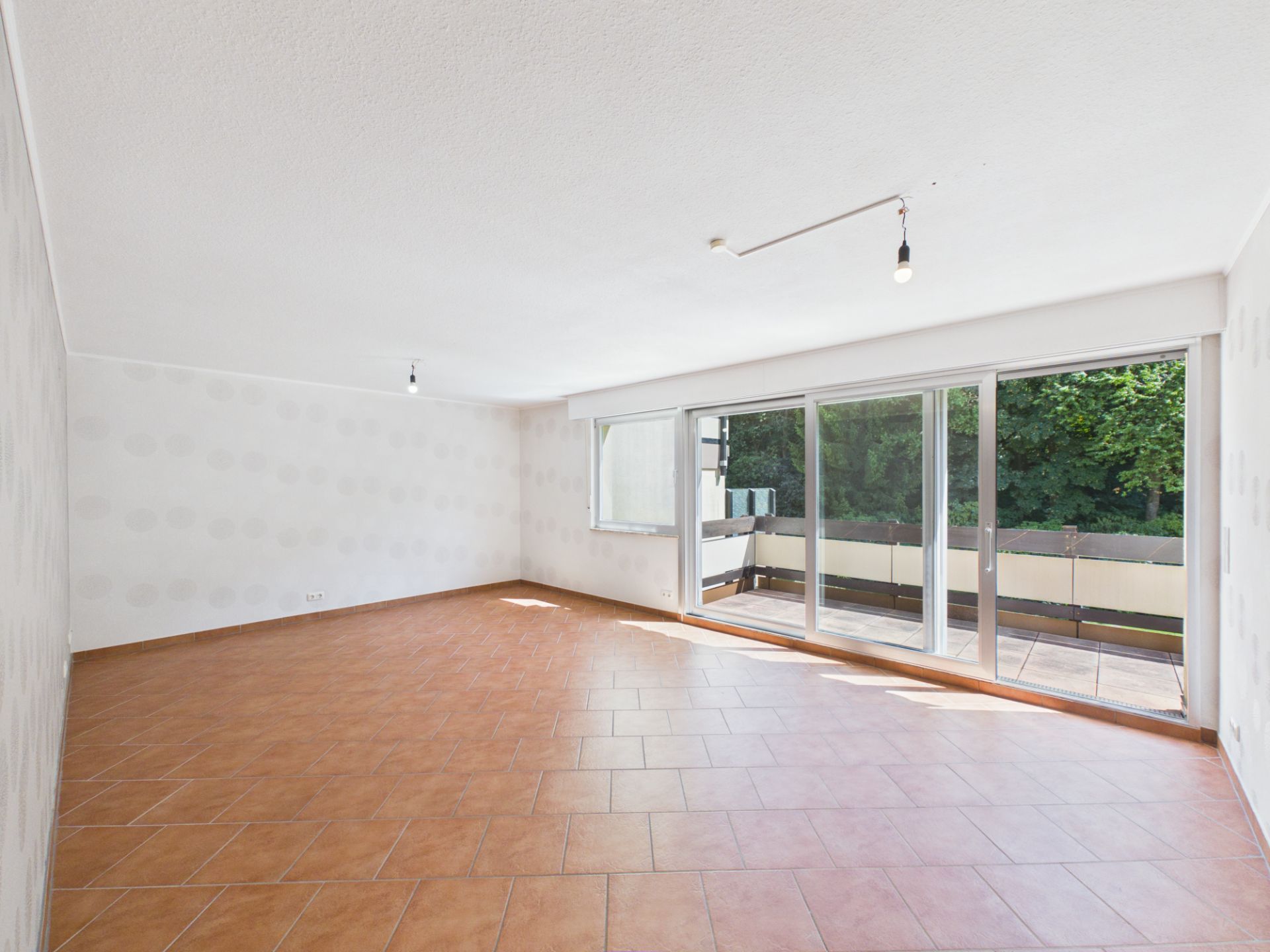 Leerer Raum mit Fliesenboden und großer Fensterfront zu einem Balkon.