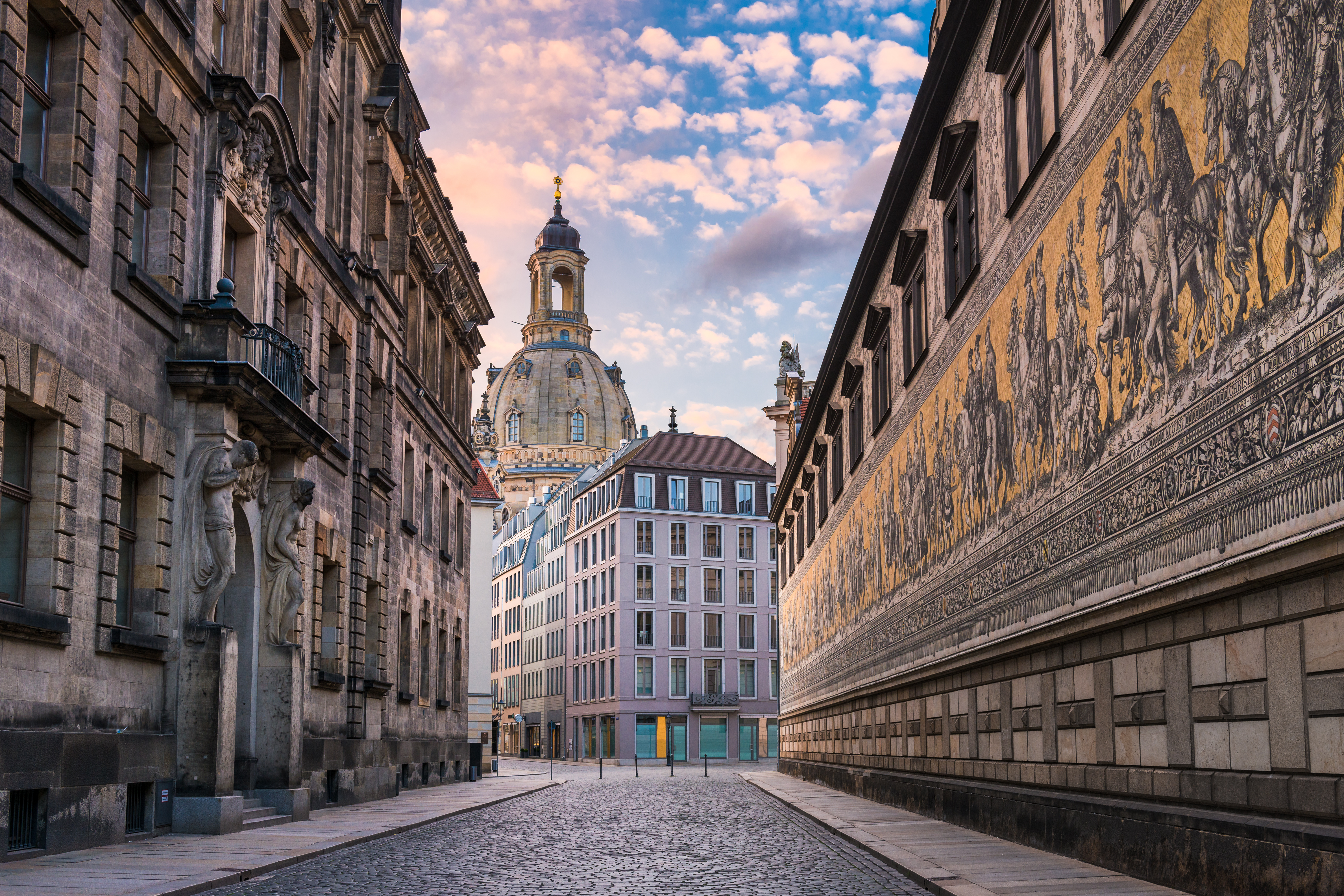 Eine gepflasterte Straße zwischen historischen Gebäuden mit einer Kuppel im Hintergrund bei Sonnenaufgang.
