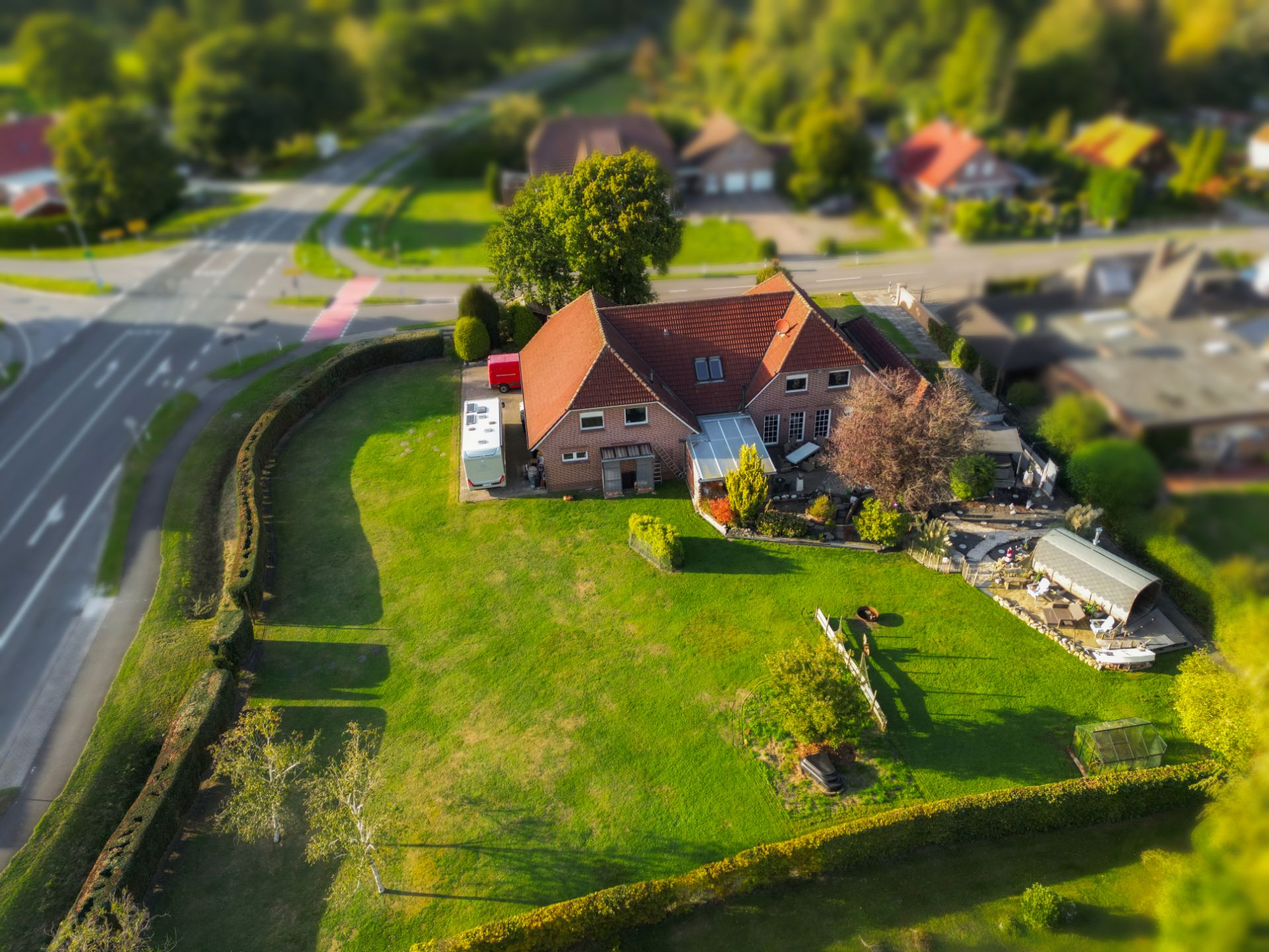 Luftaufnahme eines Einfamilienhauses mit großem Garten neben einer Straße.