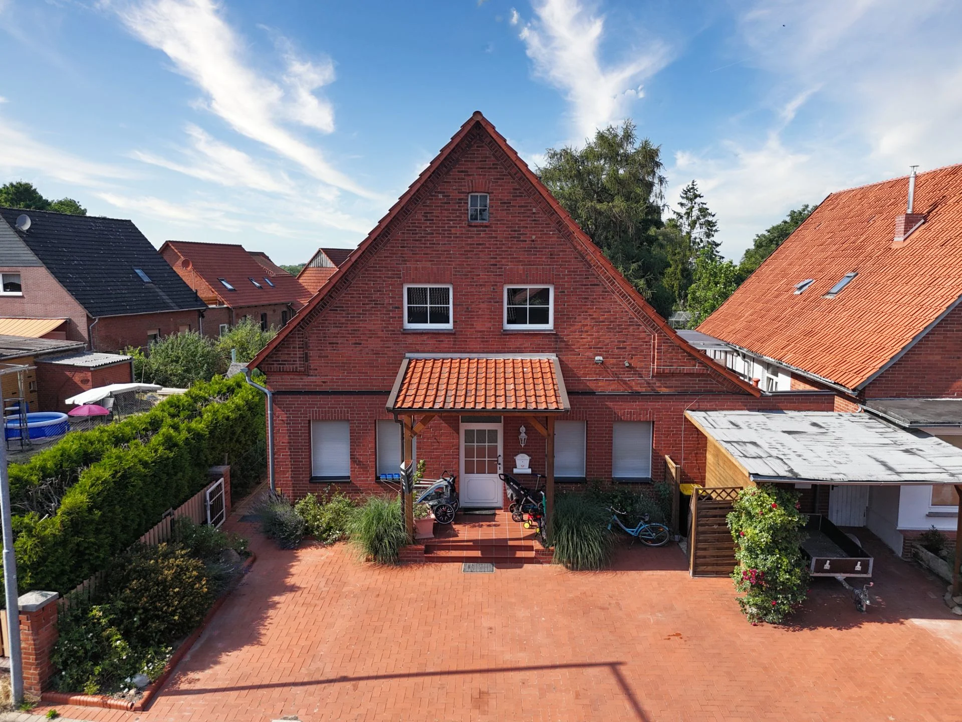 Backsteinhaus mit rotem Dach, überdachtem Eingang und Vorgarten, Fahrräder vor dem Haus.