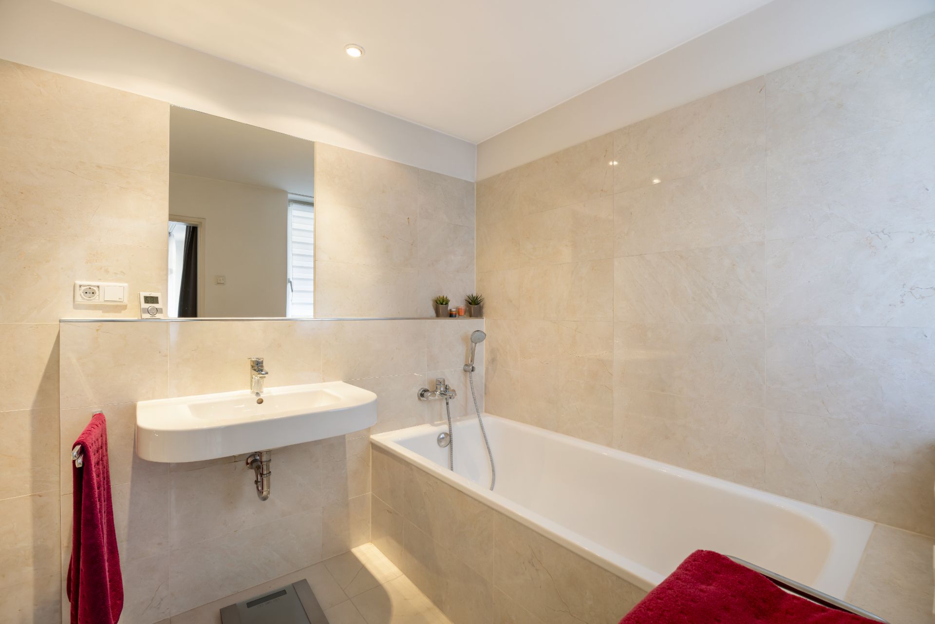 Modernes Badezimmer mit Badewanne, Waschbecken, großem Spiegel und beigem Fliesenwänden.