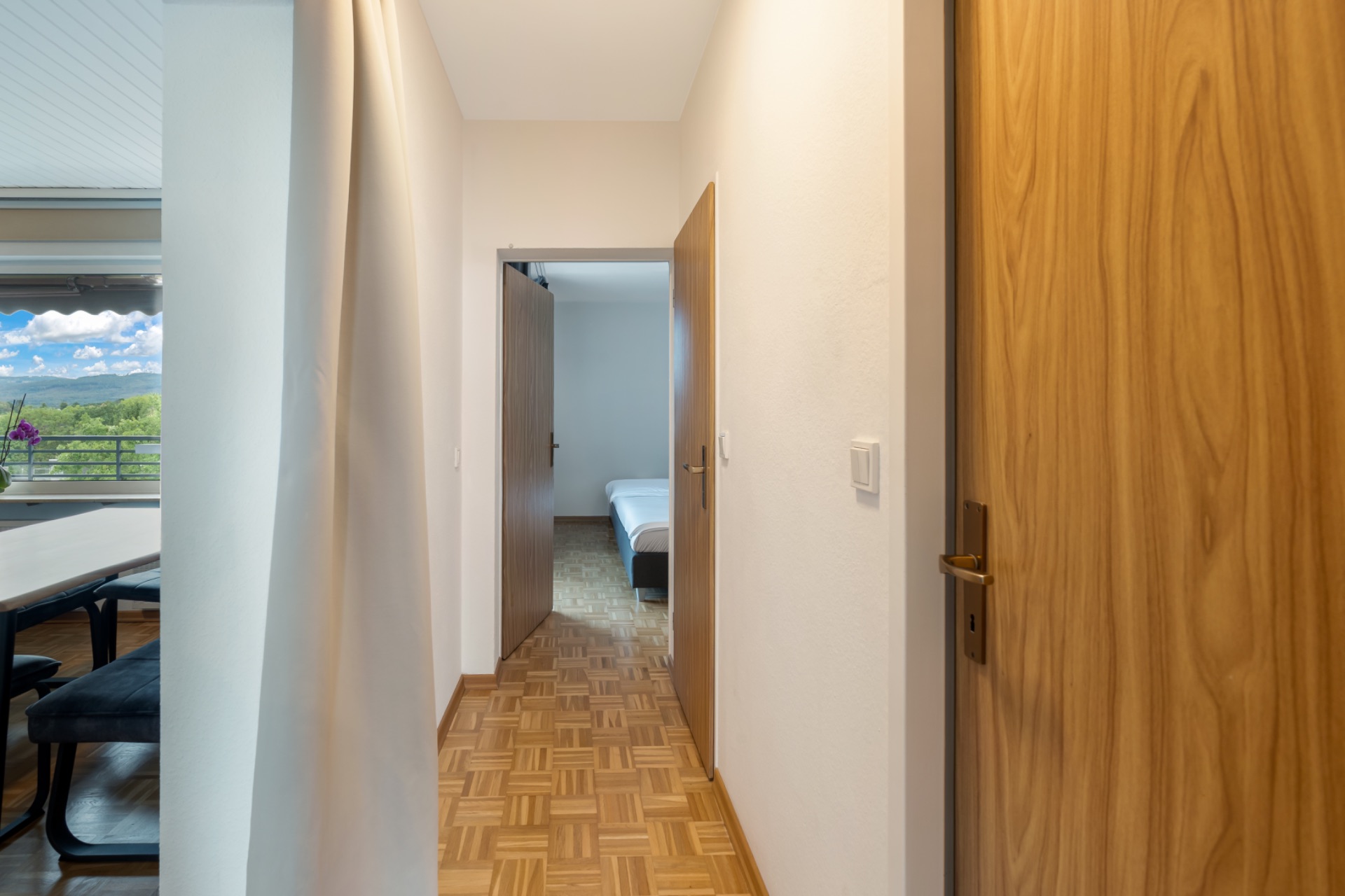Heller Flur mit Holzboden, Türen und Blick in ein Schlafzimmer mit Bett.