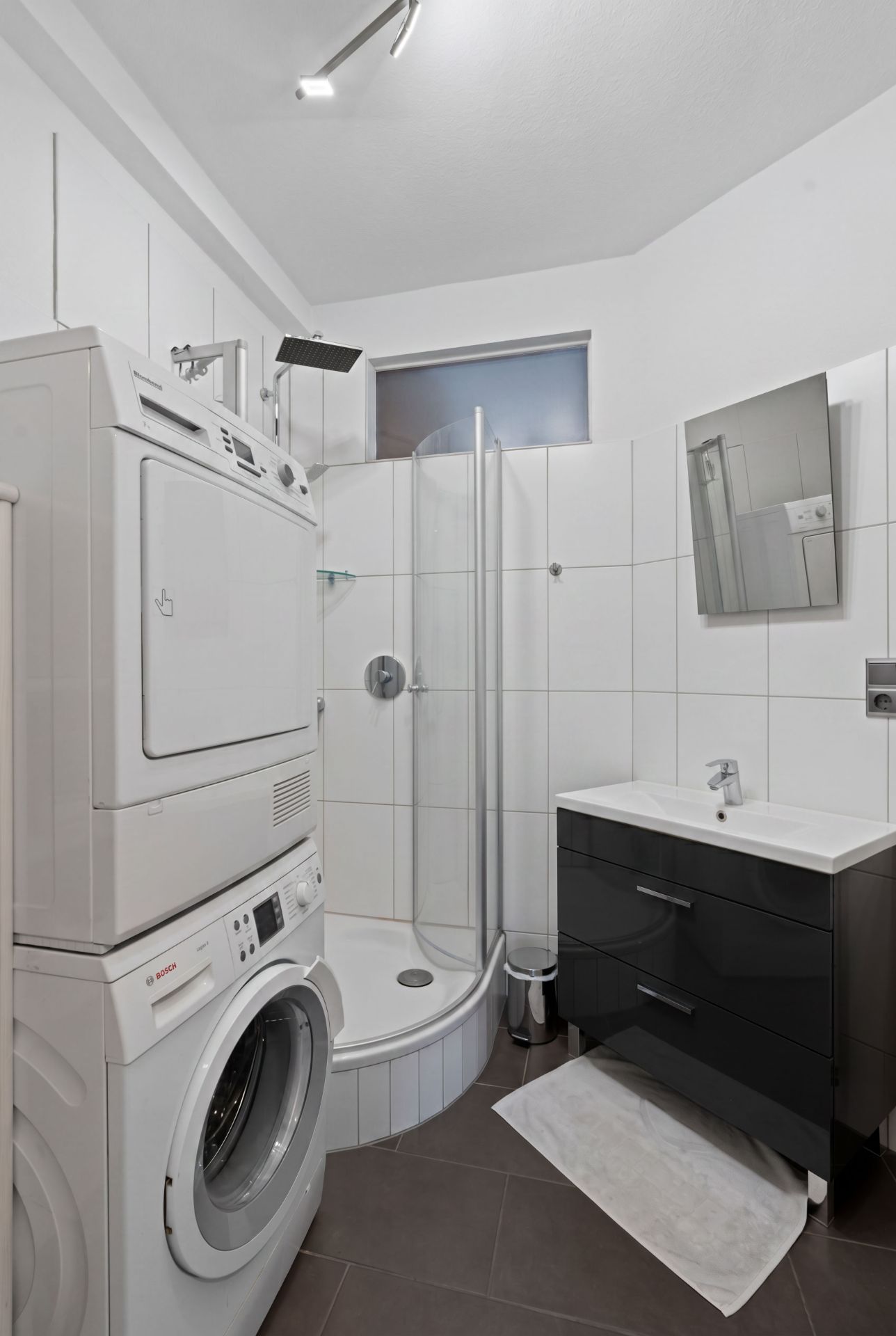 Modernes Badezimmer mit Dusche, Waschbecken, Spiegel und Waschmaschine mit Trockner.