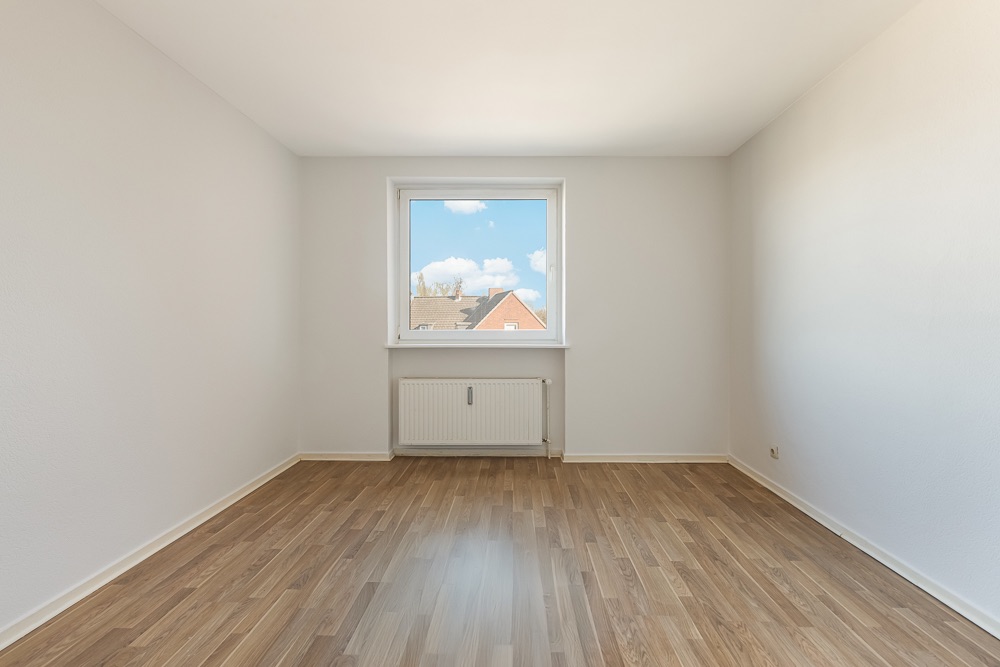 Leerer Raum mit Holzfußboden, weiß gestrichenen Wänden und Fenster mit Blick nach draußen.