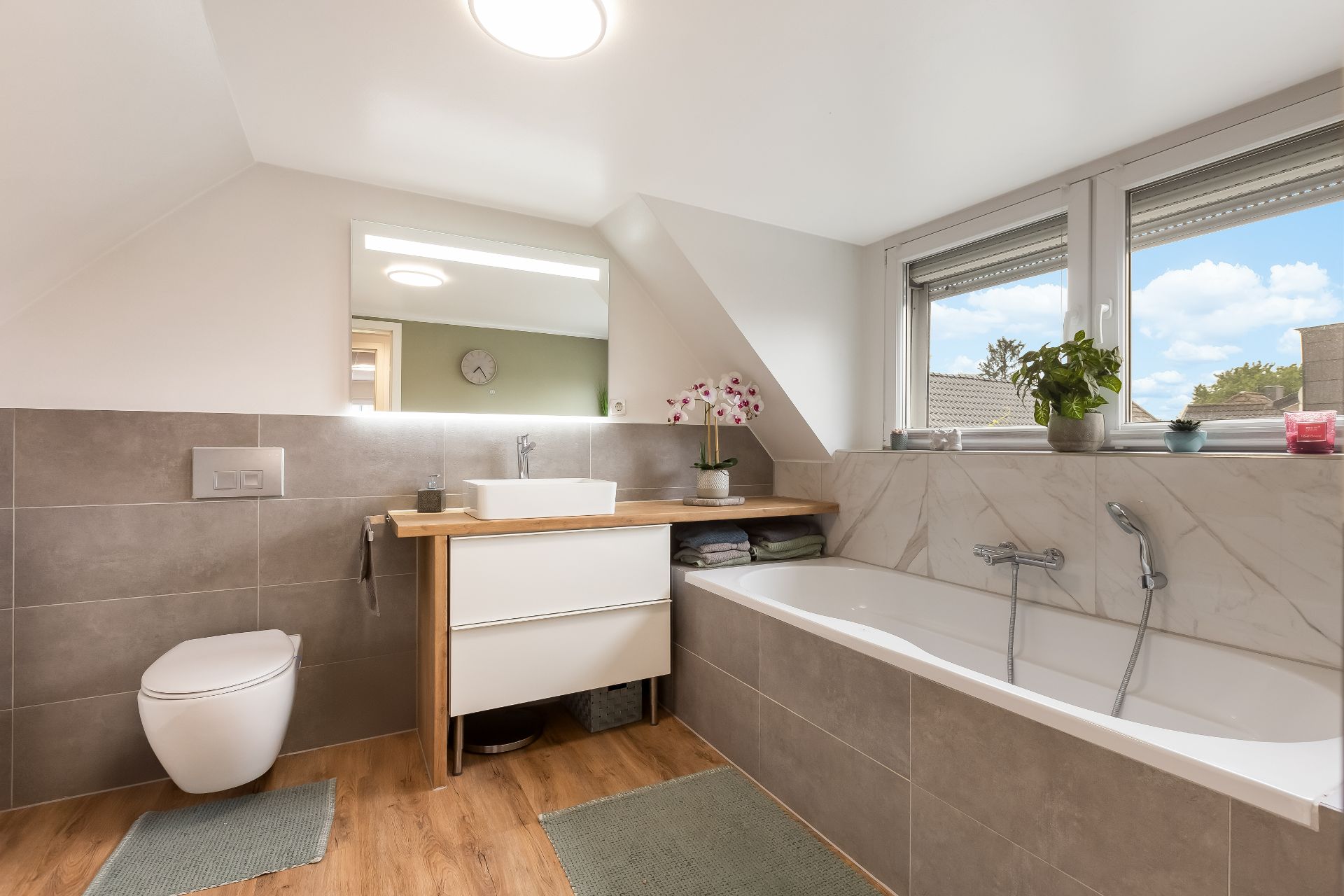 Modernes Badezimmer mit Badewanne, Waschbecken, Toilette und zwei Fenstern.