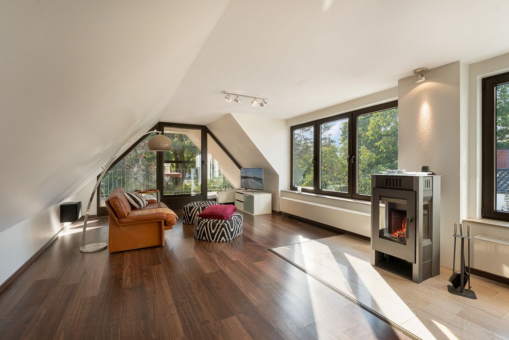 Helles Wohnzimmer mit Holzfußboden, Kamin, Sofa, großen Fenstern und Zugang zum Balkon.