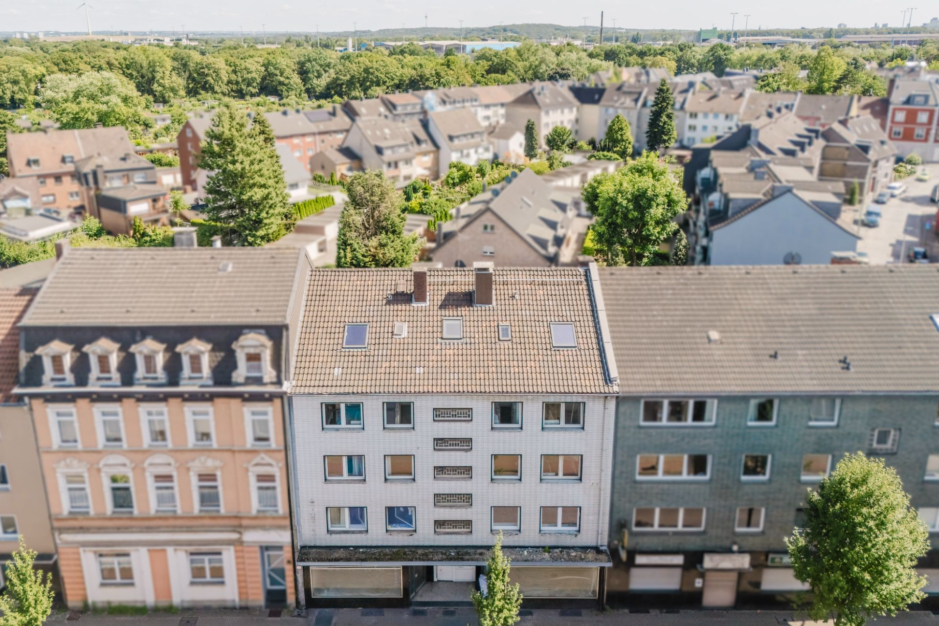 Vorderansicht eines mehrstöckigen Wohnhauses mit Bäumen und Nachbargebäuden.
