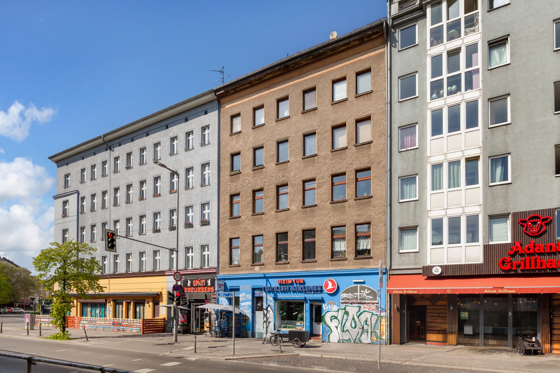 Mehrstöckige Wohnhäuser mit Geschäften im Erdgeschoss an einer belebten Straße.